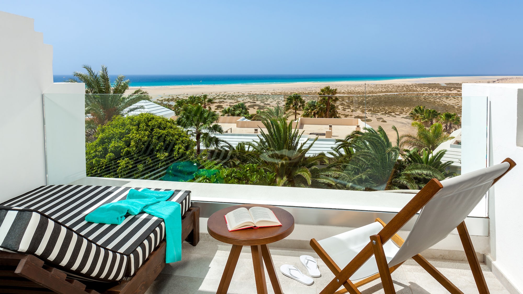 a deck with chairs and a table on a balcony overlooking a beach