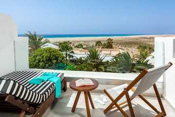 a deck with chairs and a table on a balcony overlooking a beach
