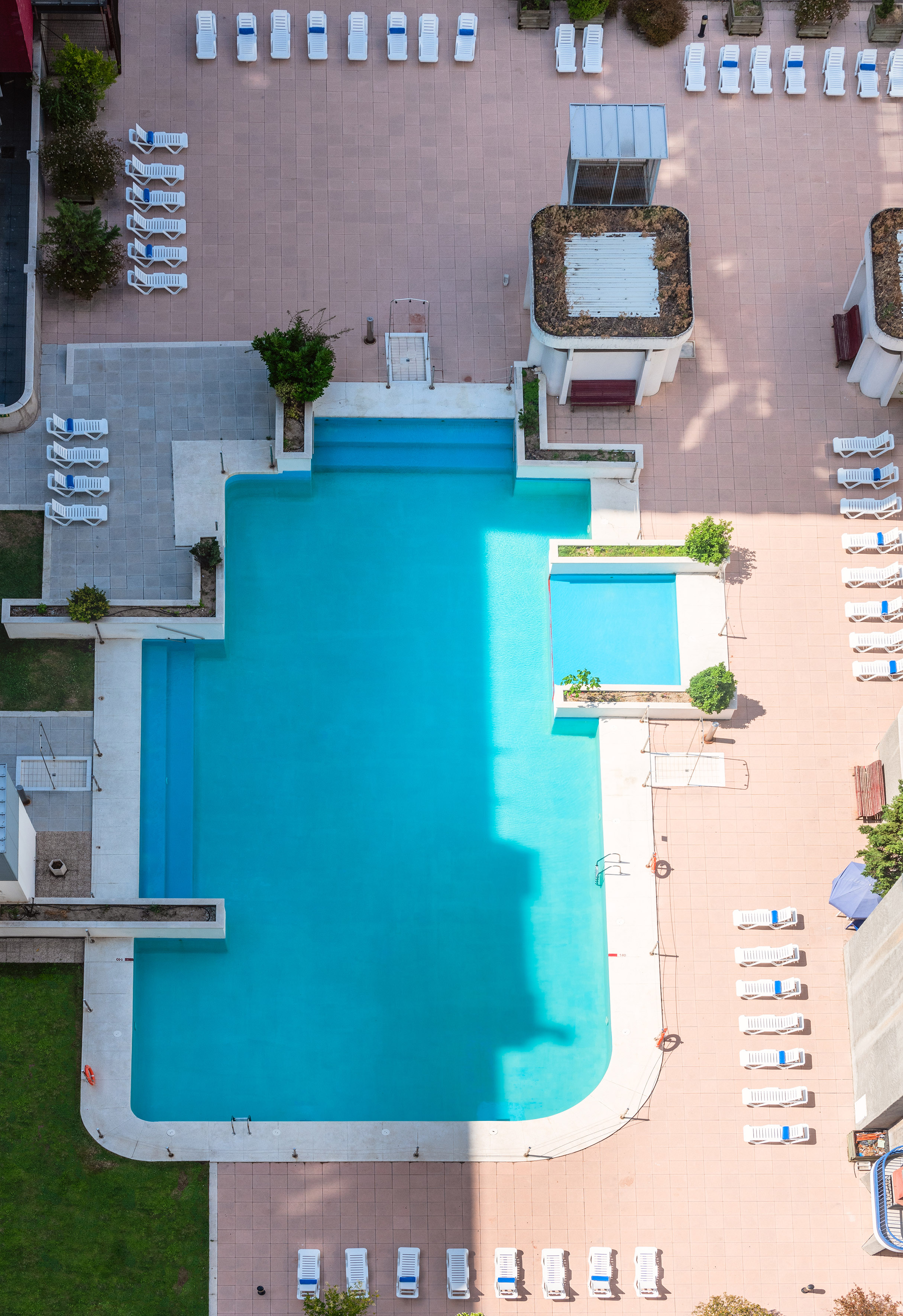 Aerial view of a resort swimming pool with white lounge chairs on a tiled patio.