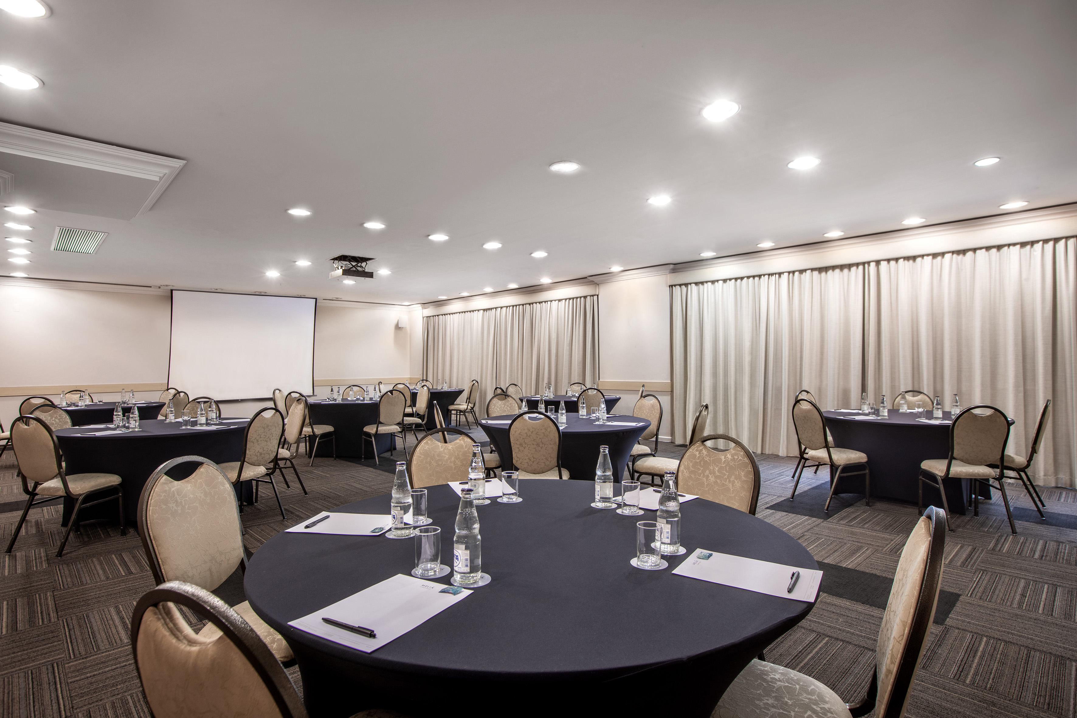 Conference room with round tables, projector screen, and meeting setup.