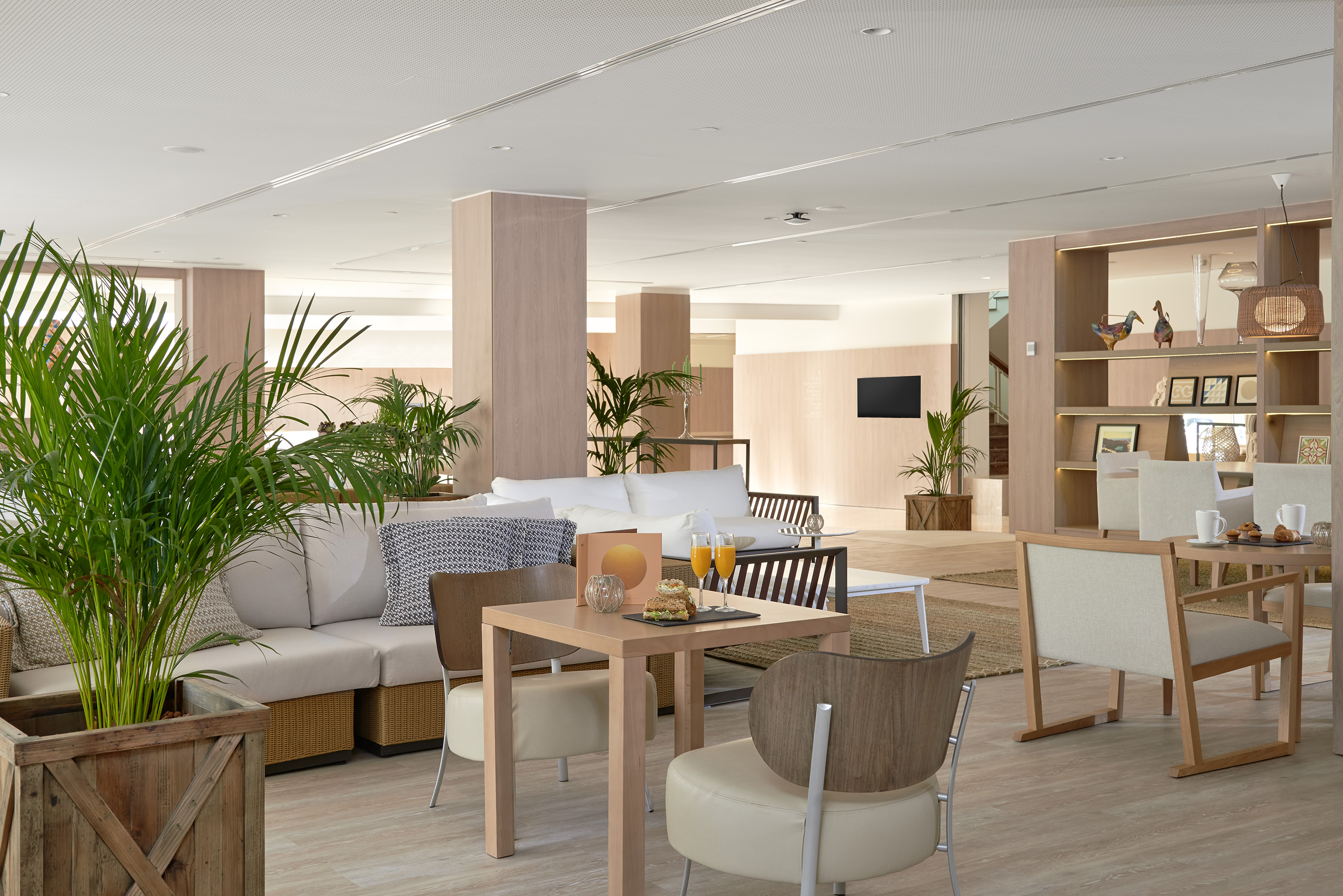 Modern hotel lobby with light wood, green plants, and comfortable seating.