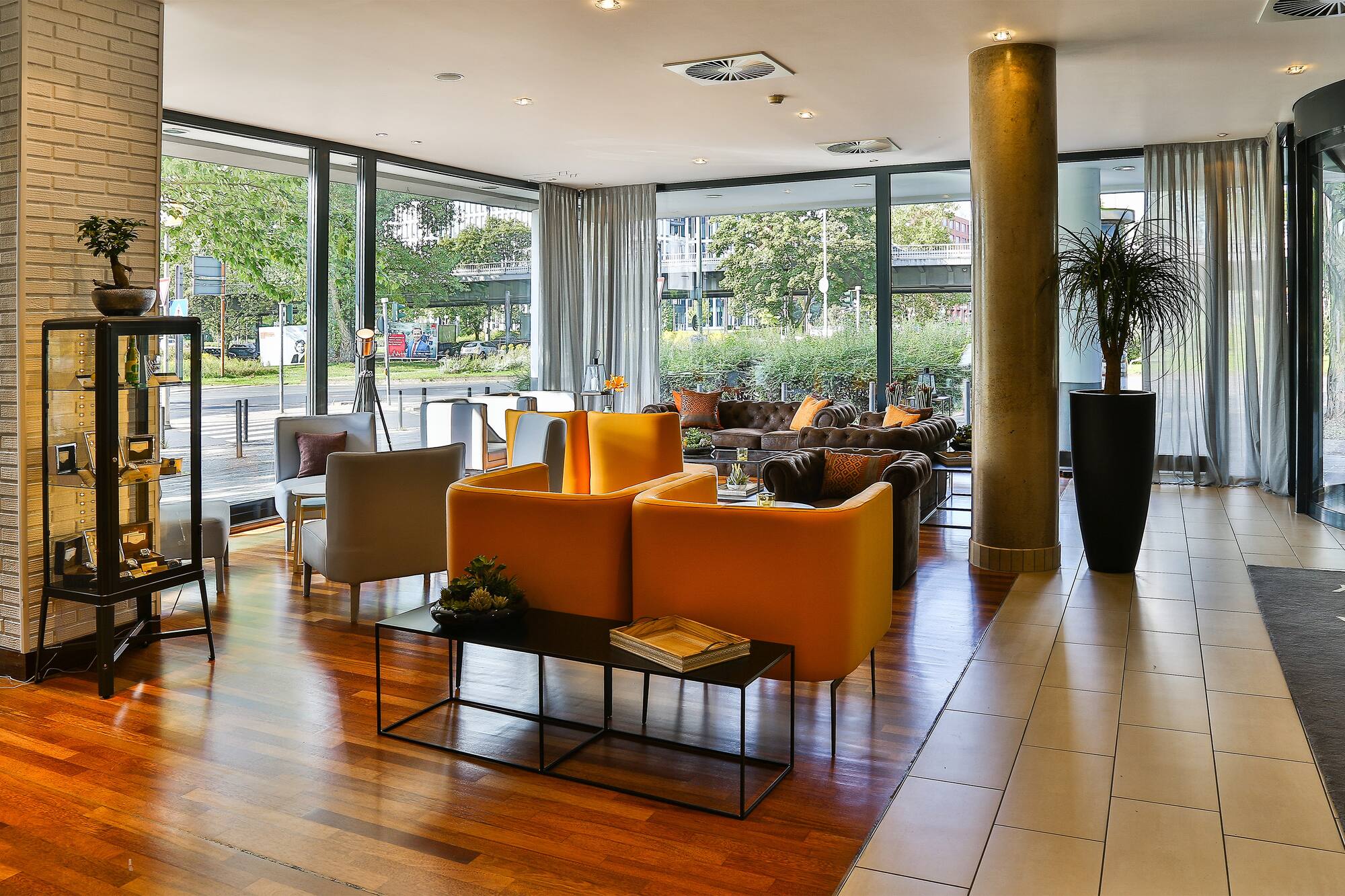 Modern hotel lounge with orange and brown seating, large windows, urban view.