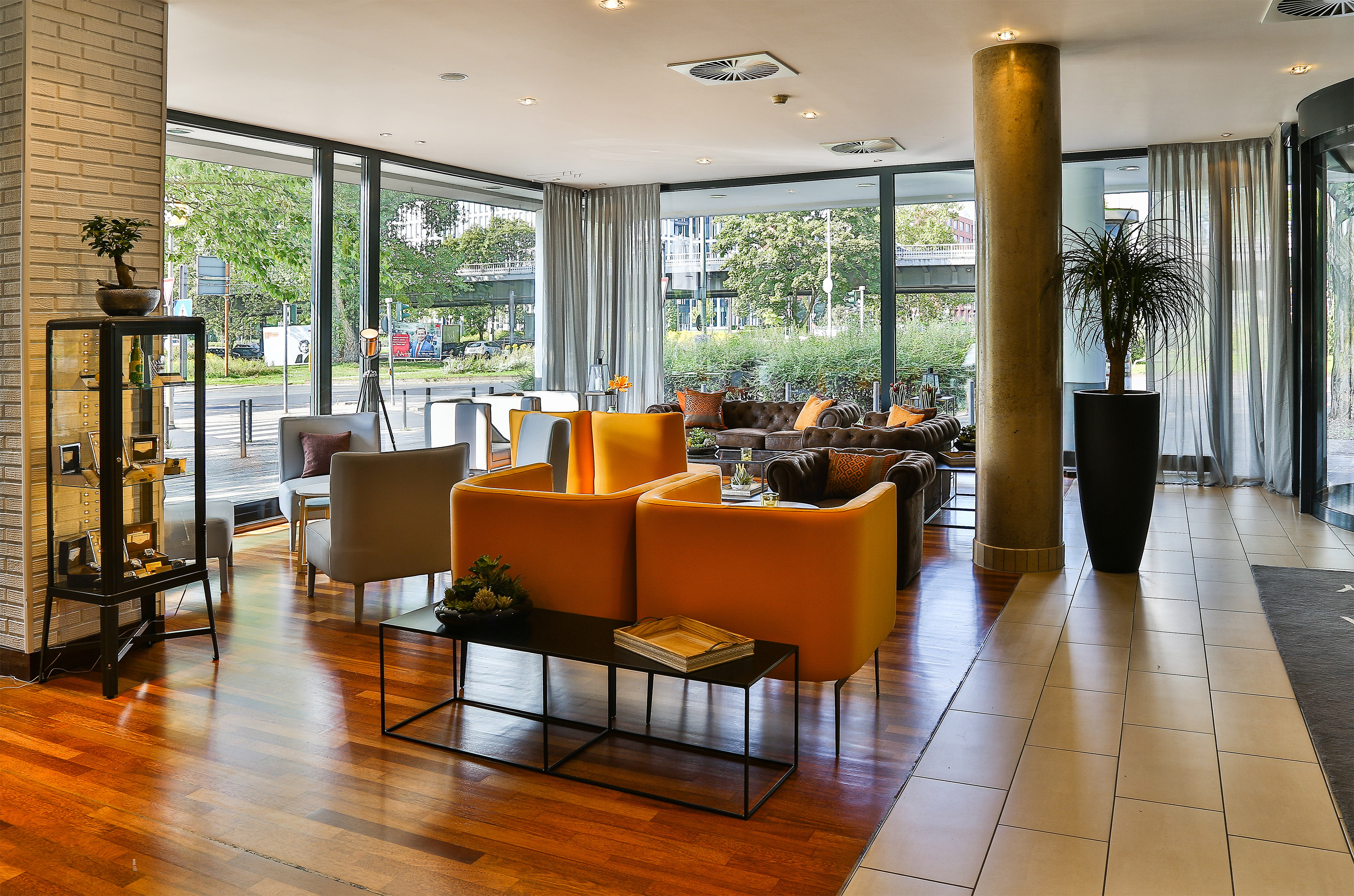 Modern hotel lounge with orange and brown seating, large windows, urban view.