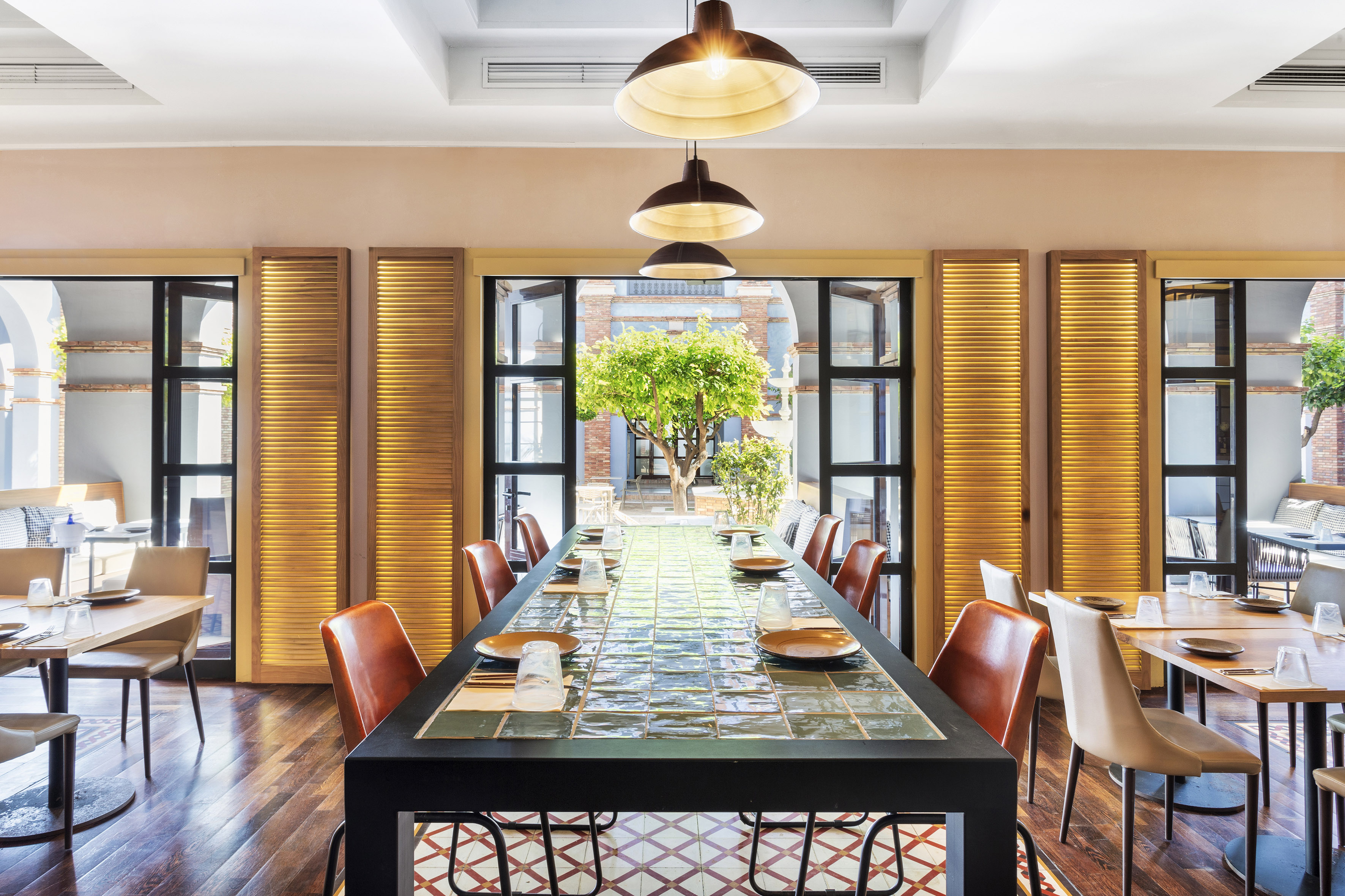 Restaurant dining room, long tiled table, leather chairs, courtyard garden view.