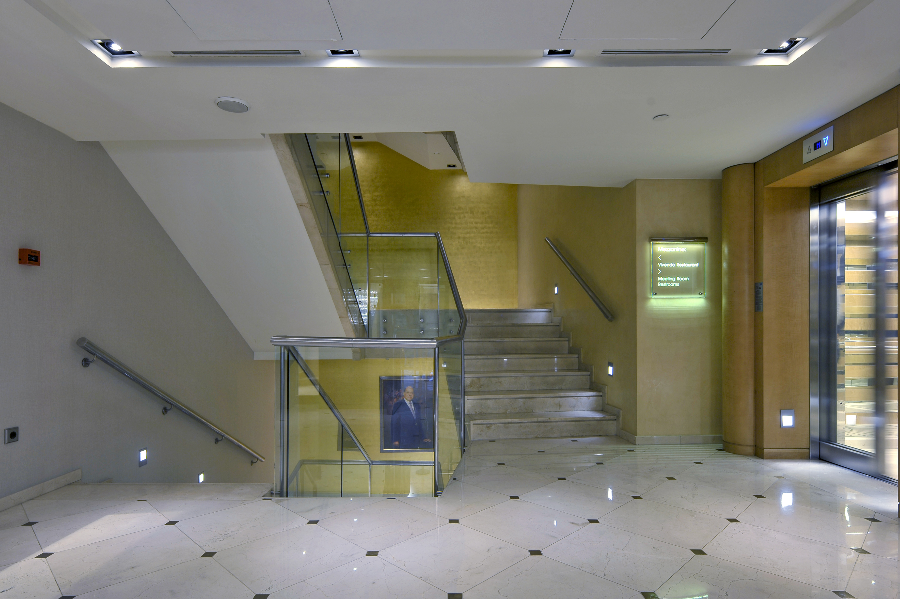 Modern hotel lobby interior with marble stairs, glass railing, and elevator.
