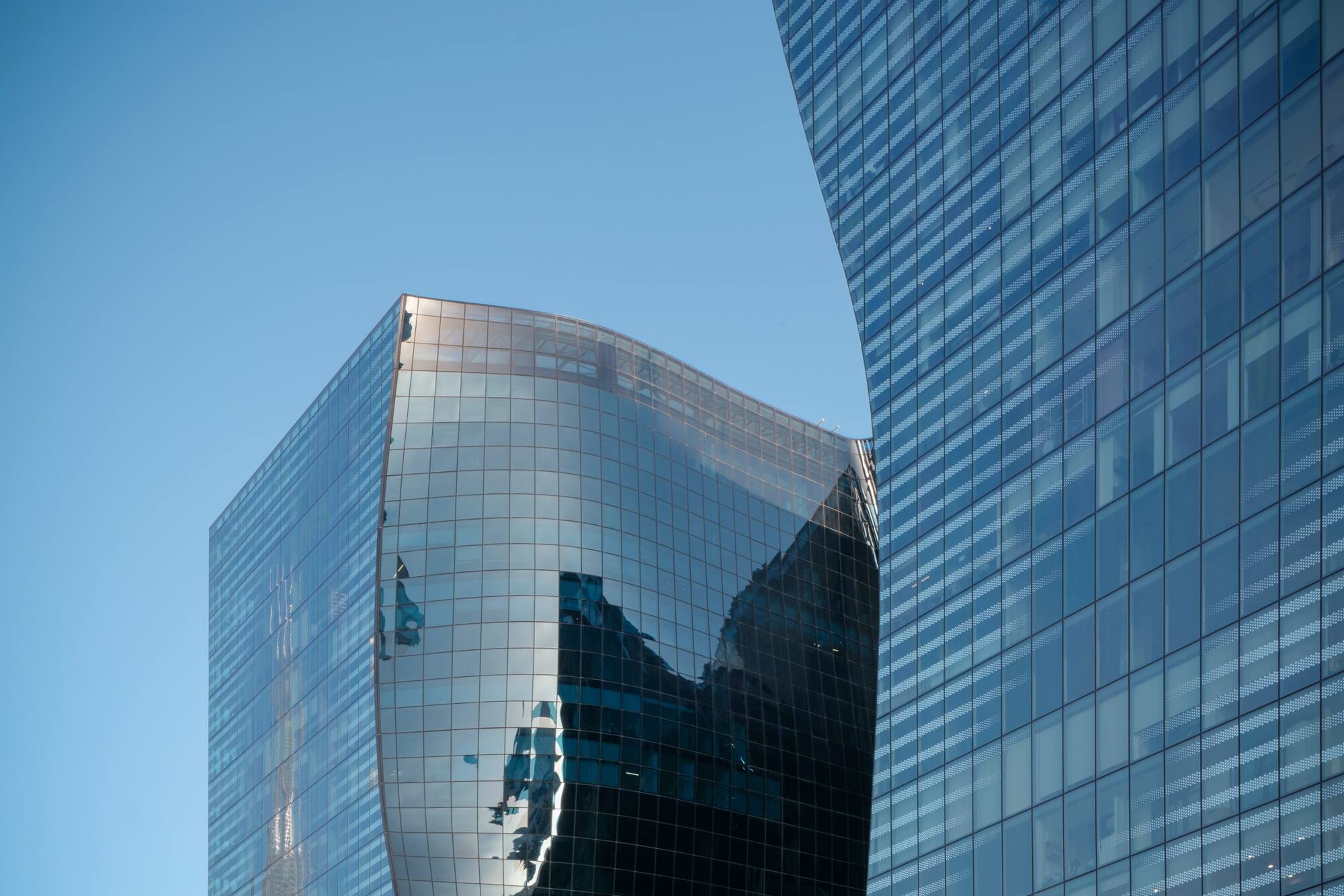 Curved glass skyscrapers reflecting blue sky, modern architectural design.
