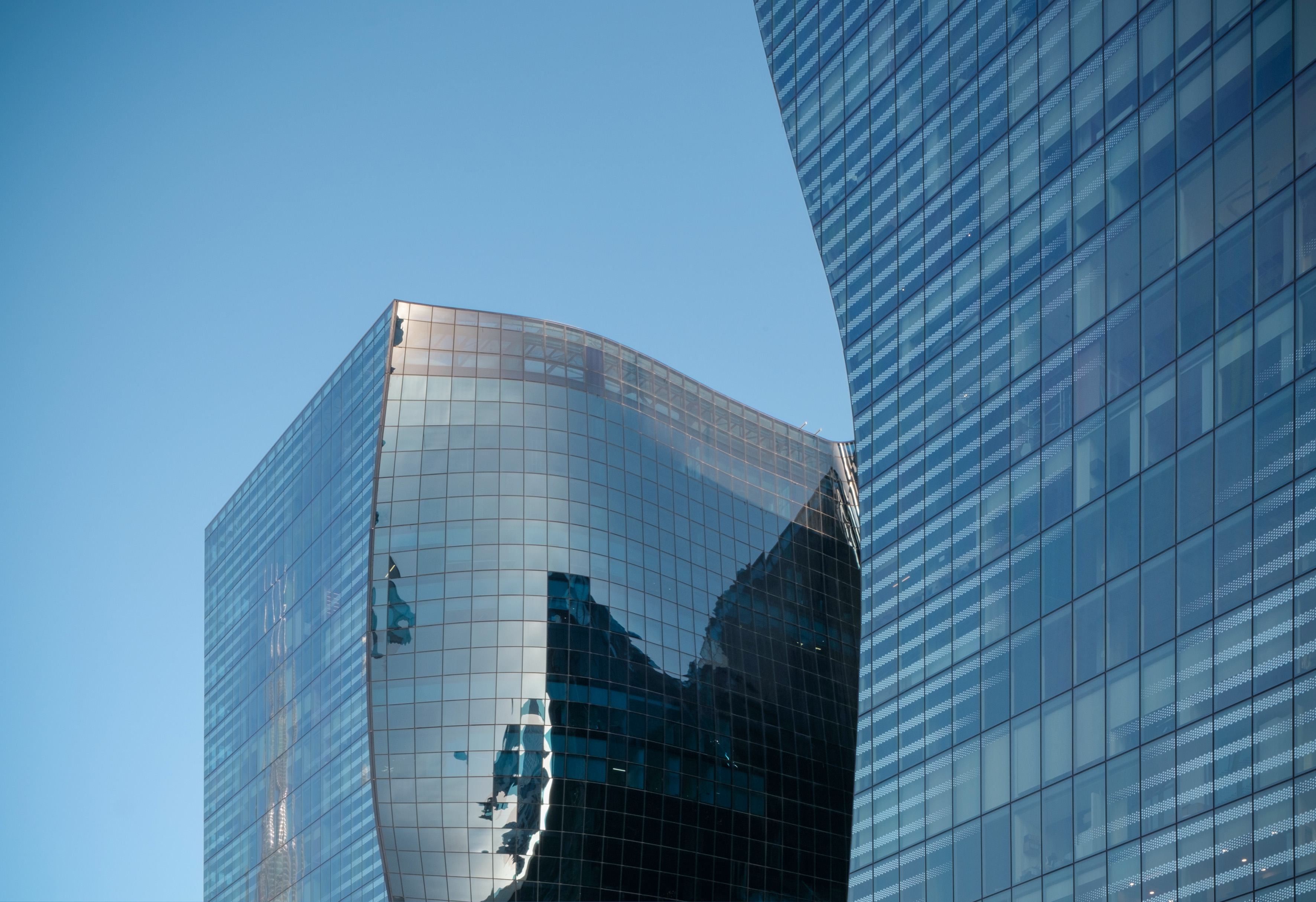 Curved glass skyscrapers reflecting blue sky, modern architectural design.