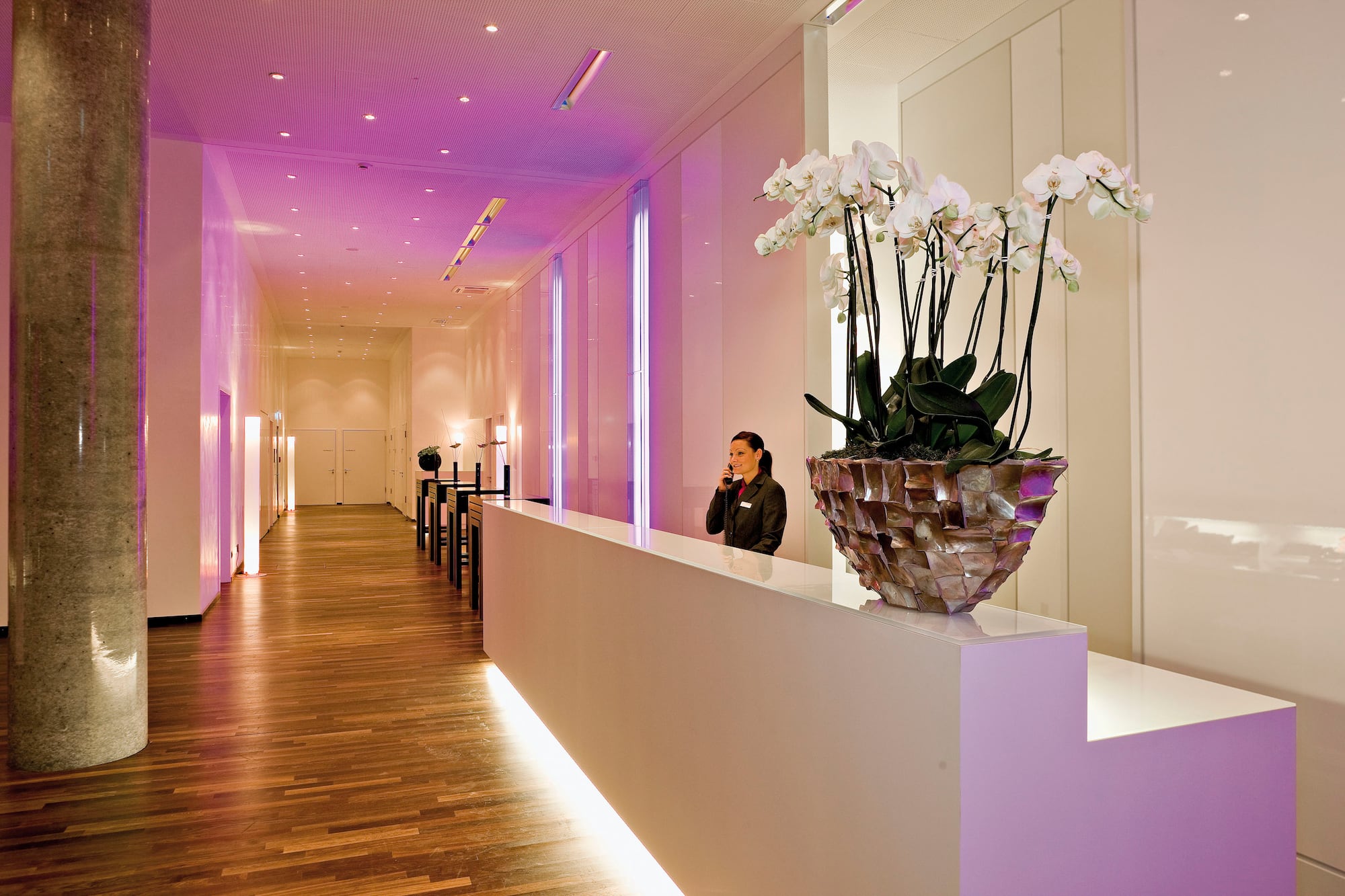 Hotel receptionist at modern desk with white orchids and purple ambient lighting.