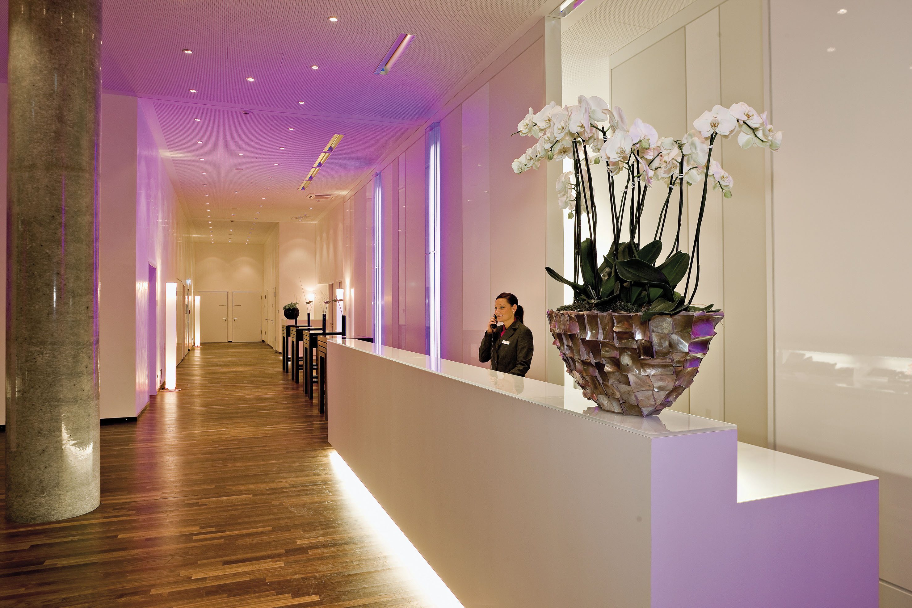 Hotel receptionist at modern desk with white orchids and purple ambient lighting.