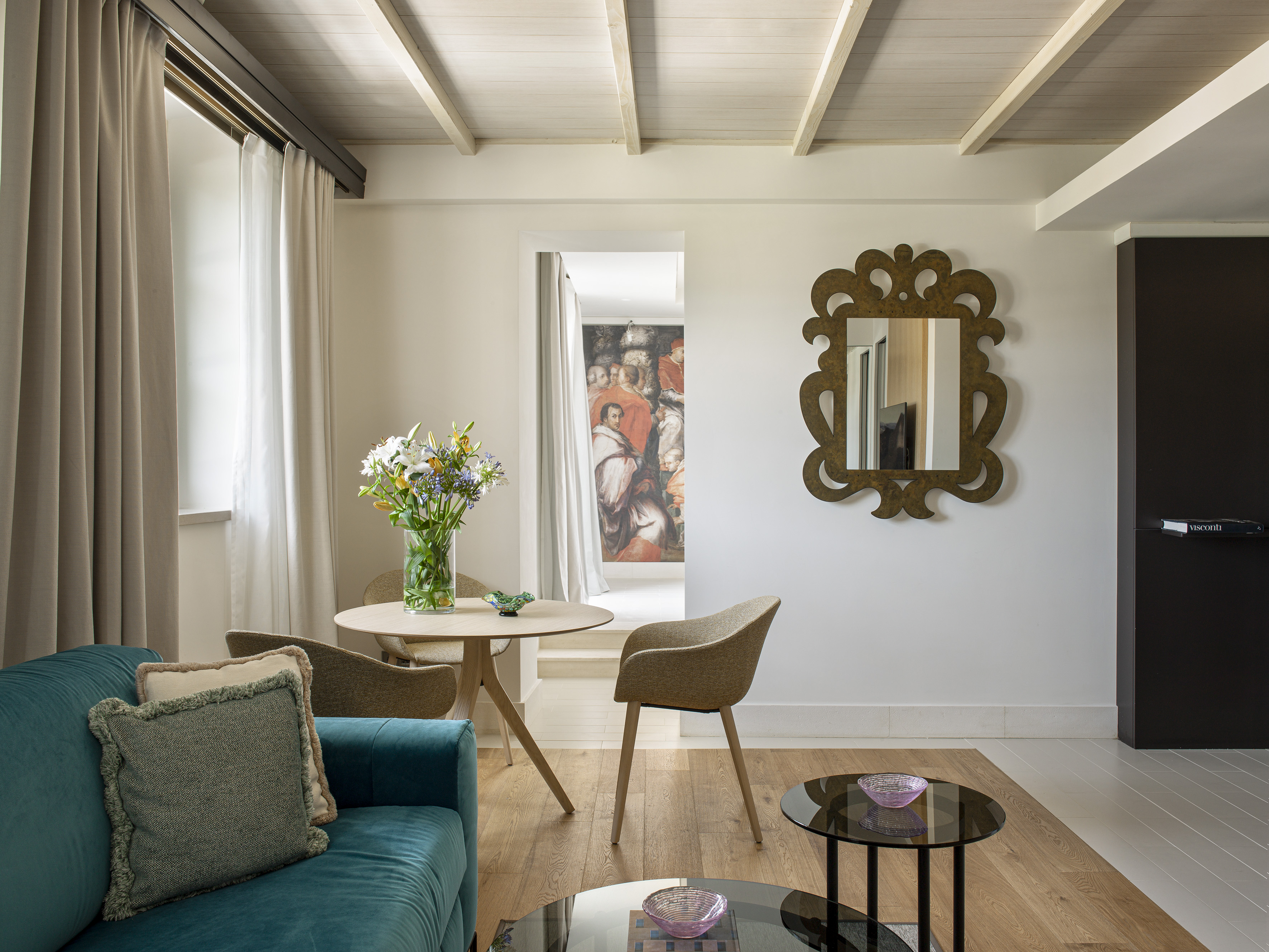 Modern living room with teal sofa, dining area, wooden floor, and ornate mirror.