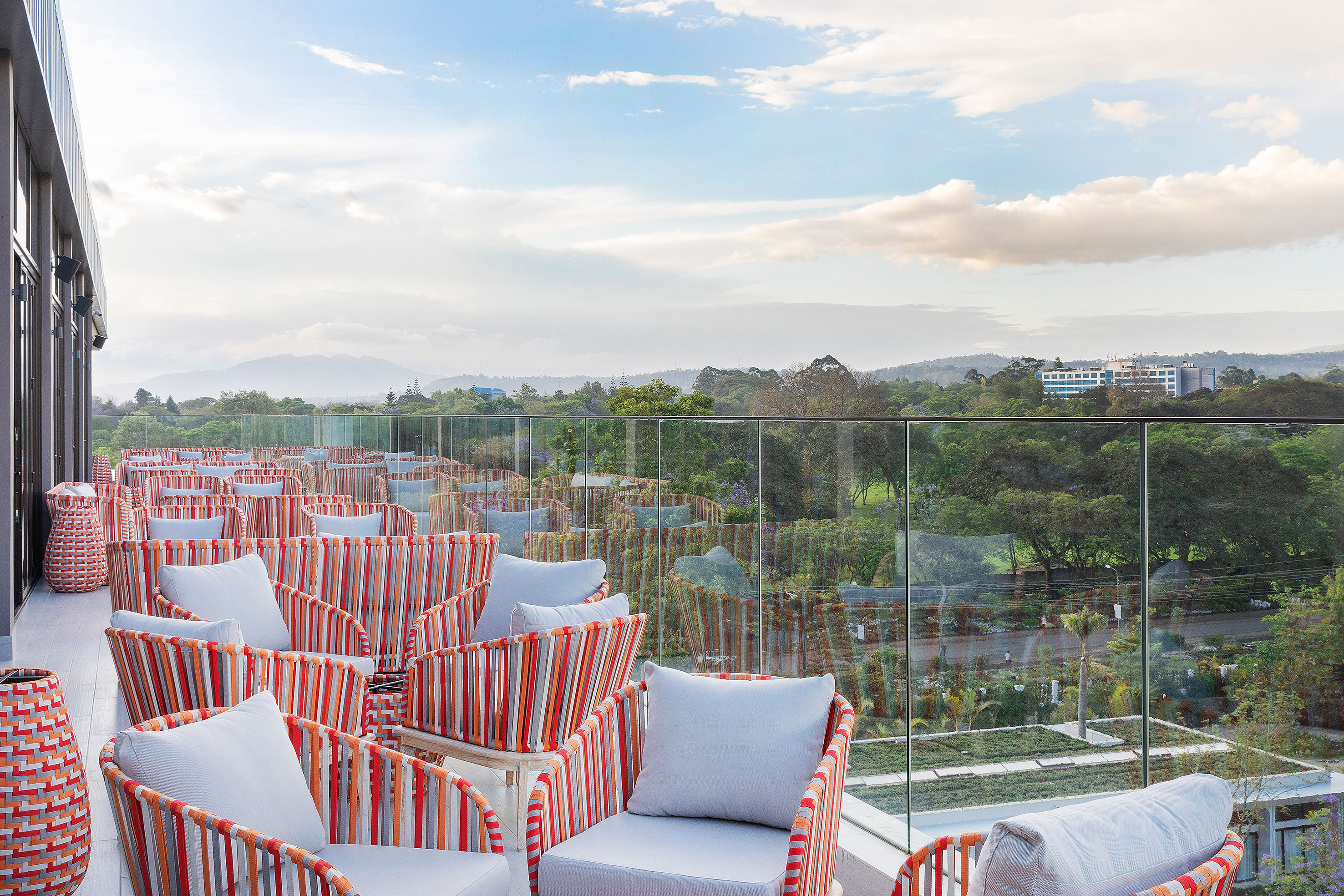 Rooftop terrace with colorful outdoor seating, glass railing, and scenic green landscape.