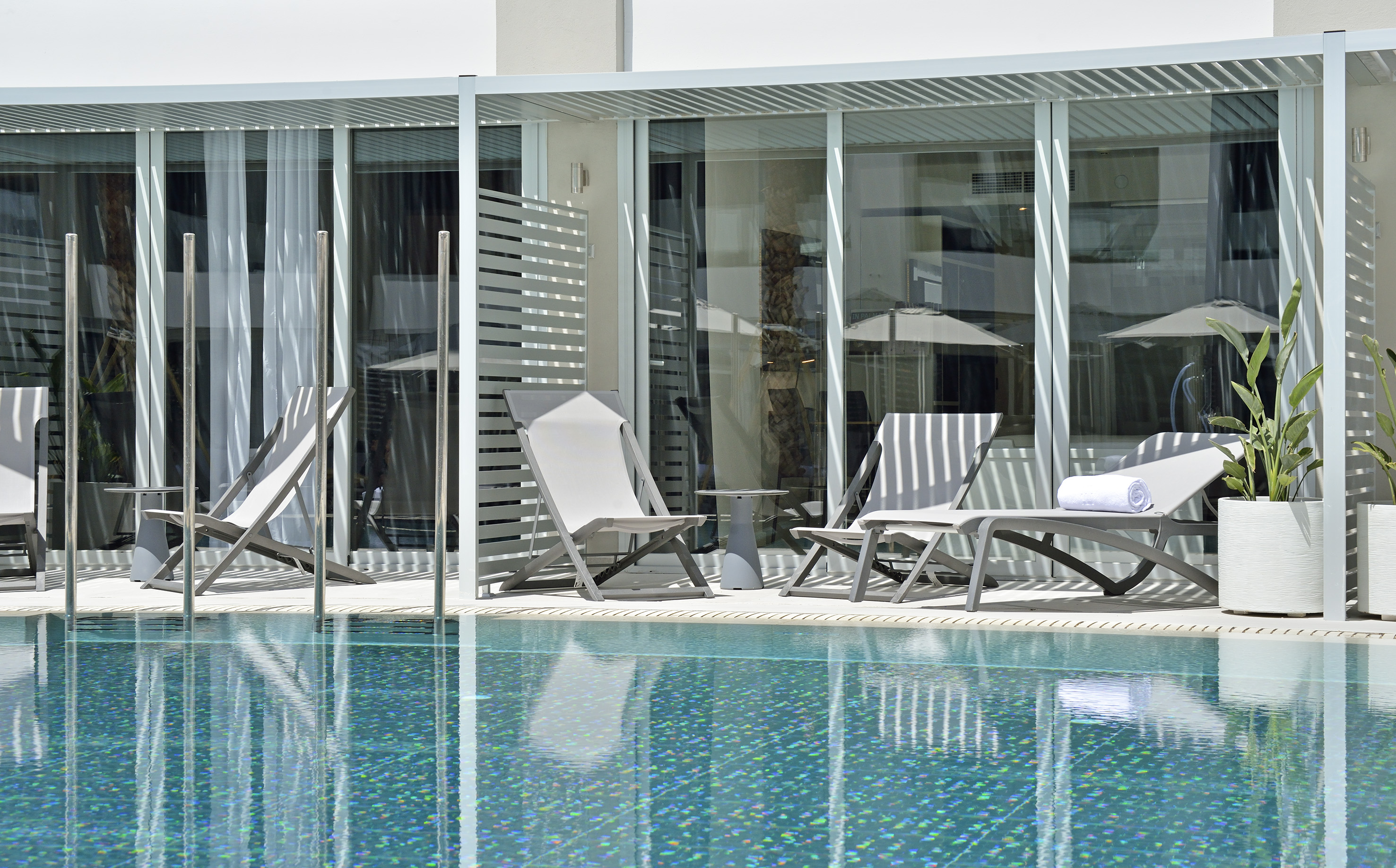 Outdoor hotel patio with modern lounge chairs, swimming pool, and white pergola.