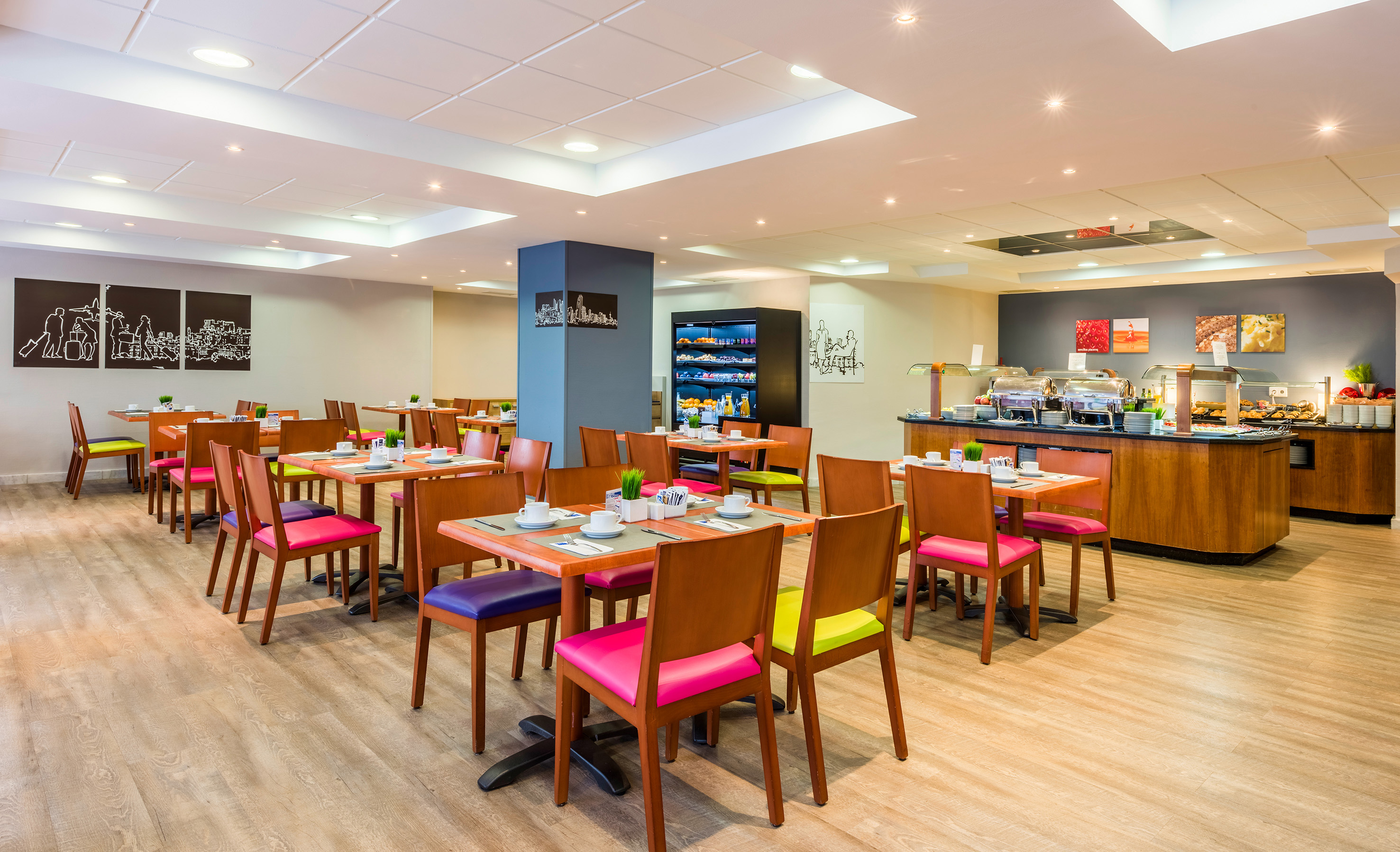 Bright hotel dining room with colorful chairs, buffet station, and wood floors.