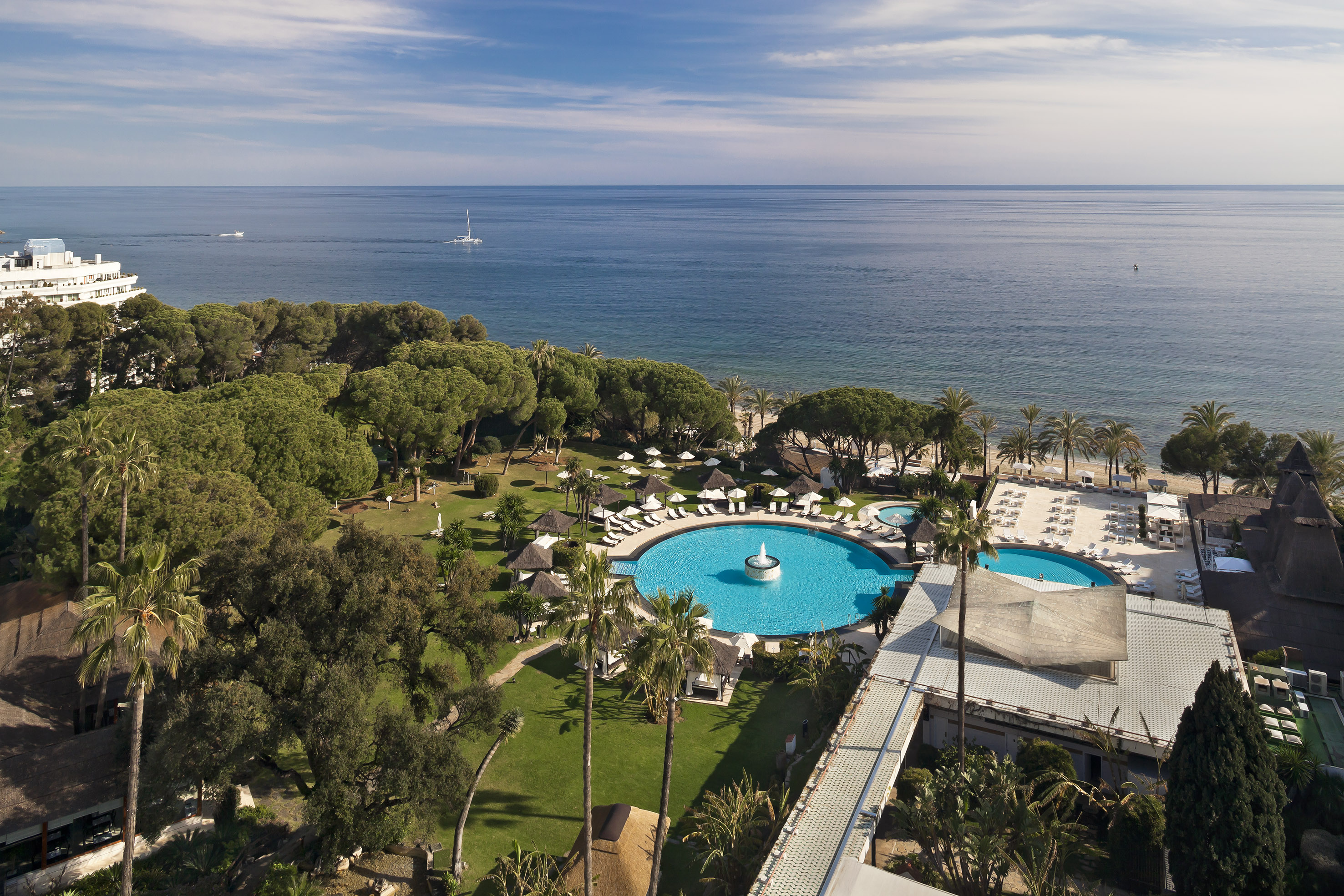 Aerial view of luxury resort with large pool, beach, ocean, and palm trees.
