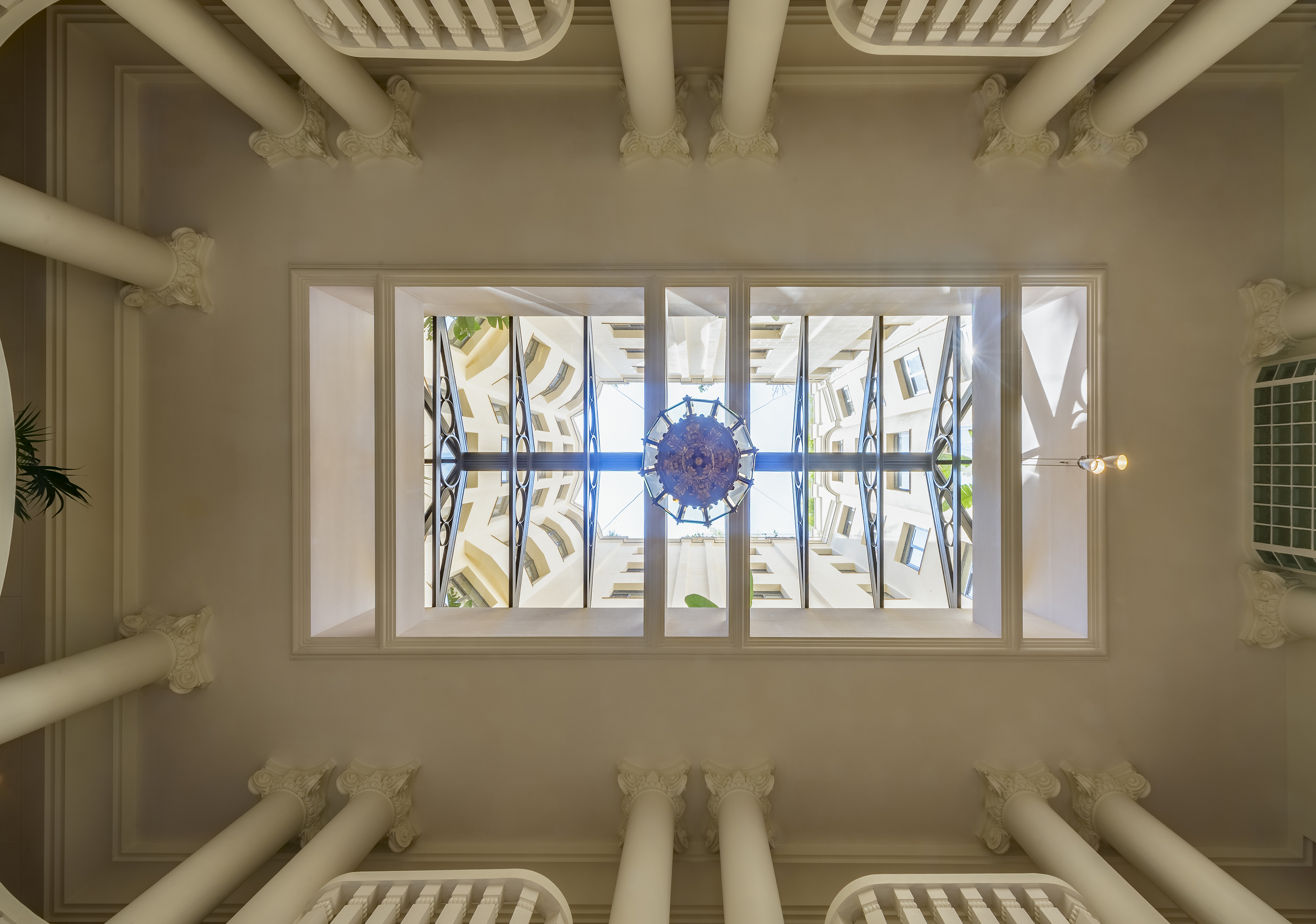 Ornate architectural ceiling with white columns, skylight, and central chandelier.