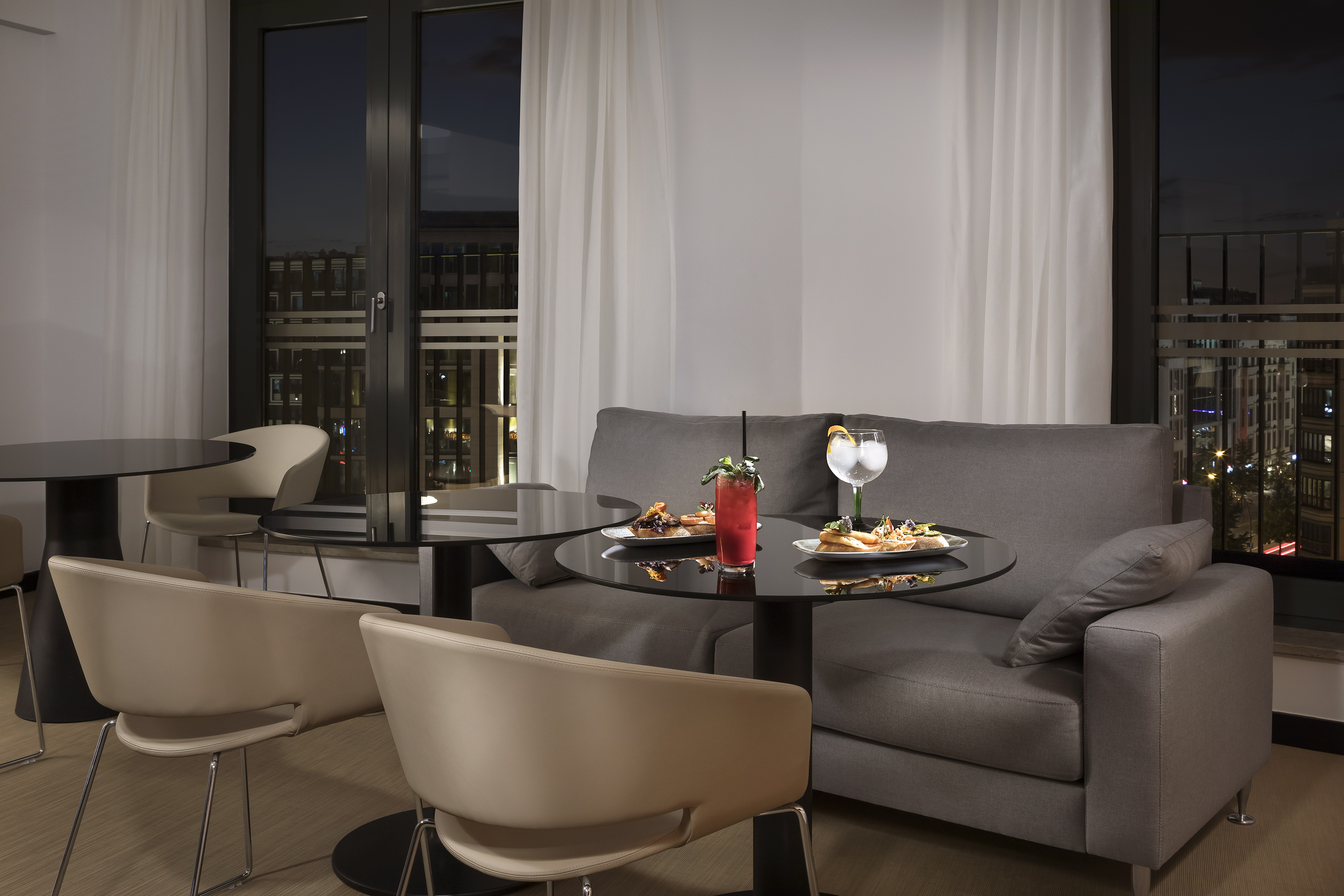 Modern hotel lounge bar with cocktails, appetizers, and city night view.