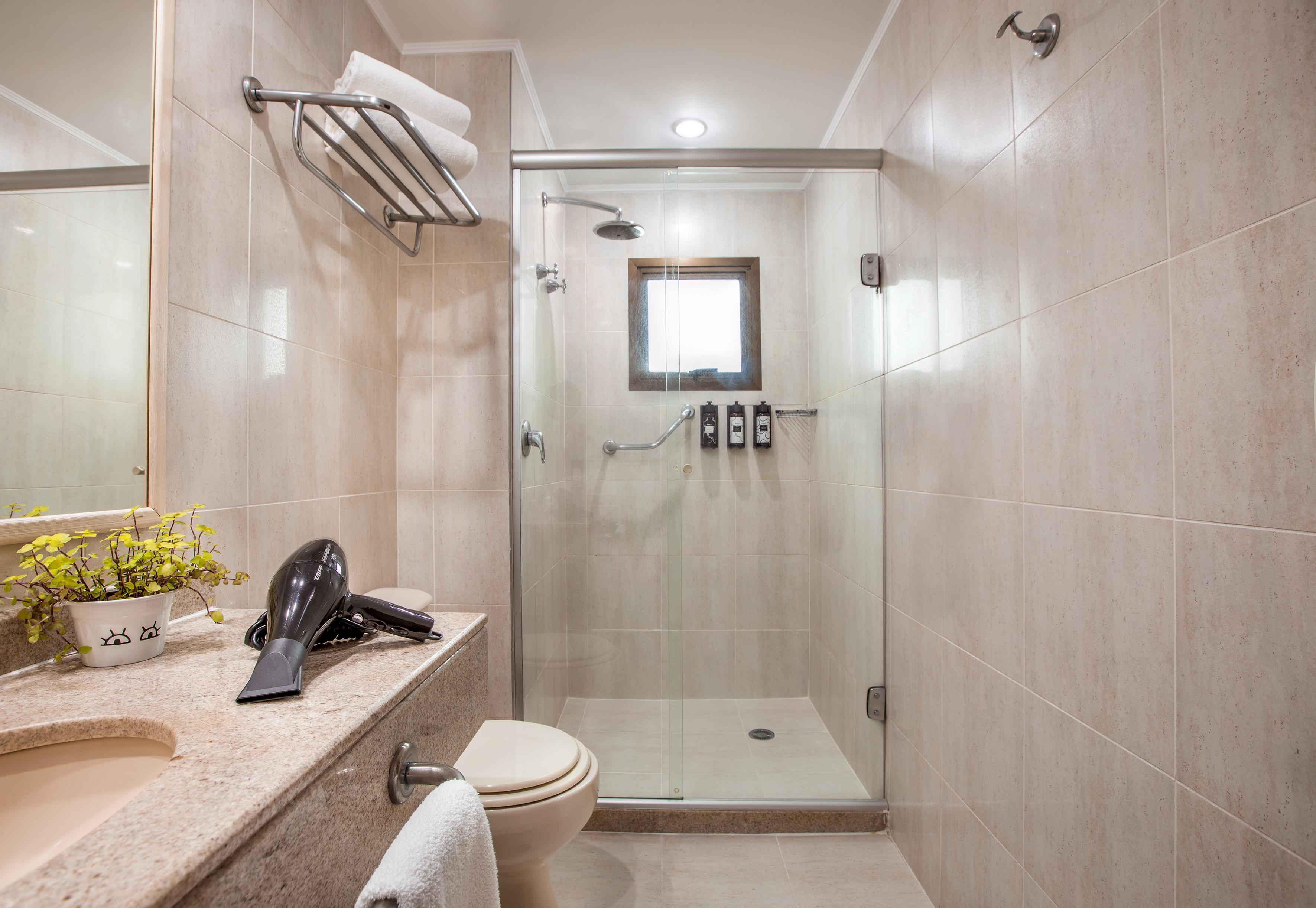 Tiled modern bathroom with glass shower, sink, toilet, and hairdryer.