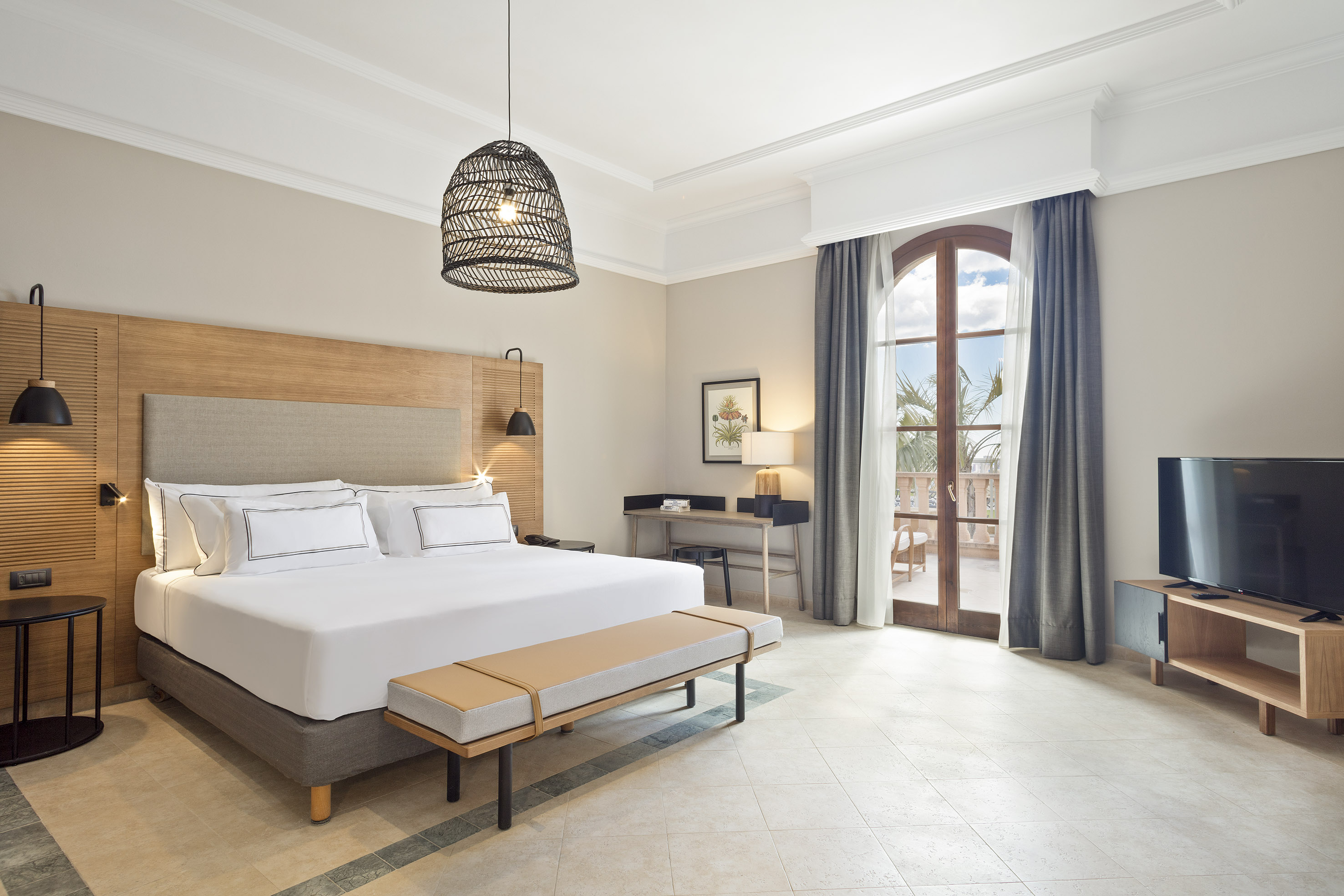 Modern hotel bedroom with king bed, desk, balcony access, and rattan pendant light.