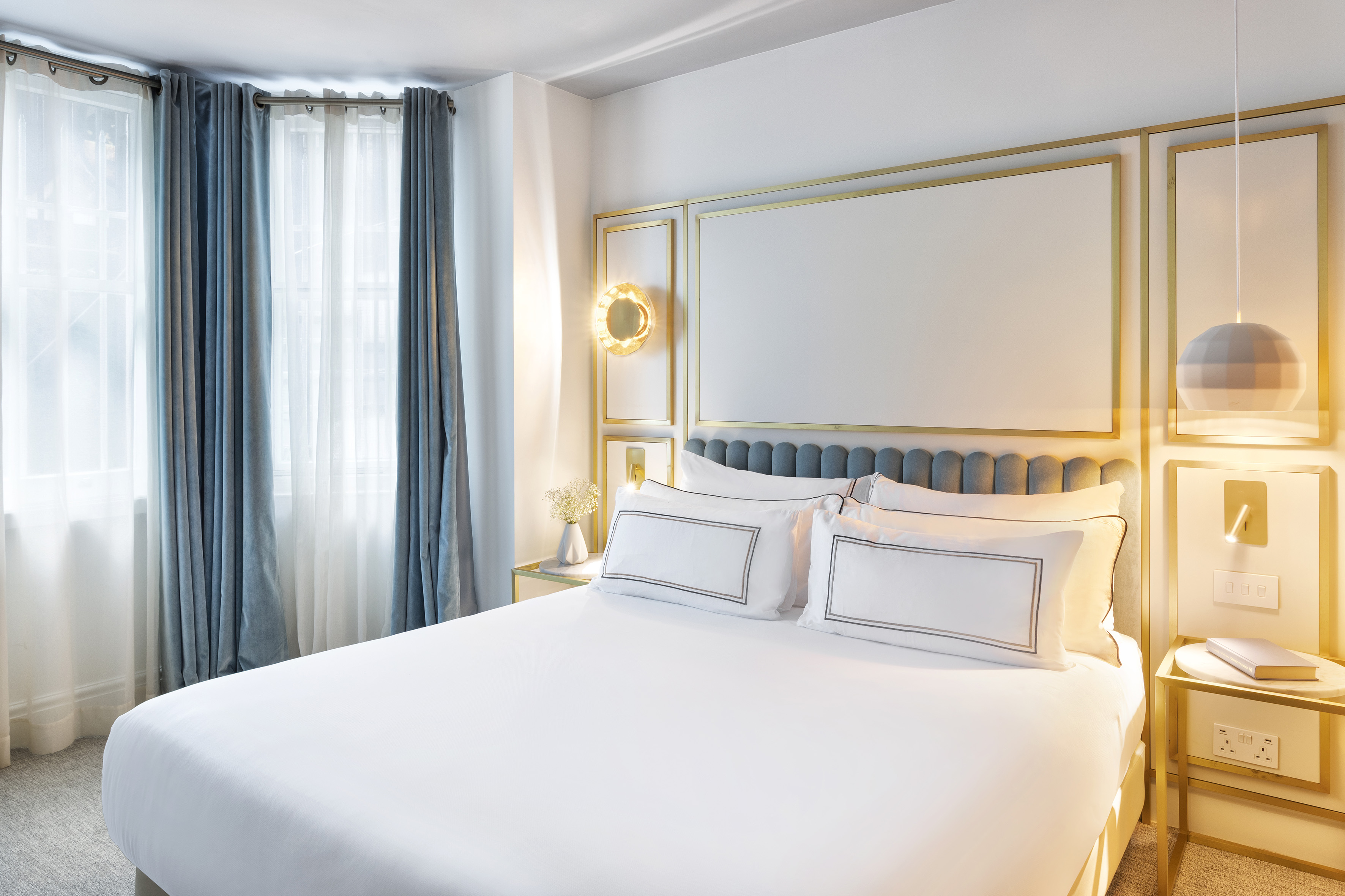 Luxurious hotel bedroom with white bed, blue velvet curtains, and gold paneling.