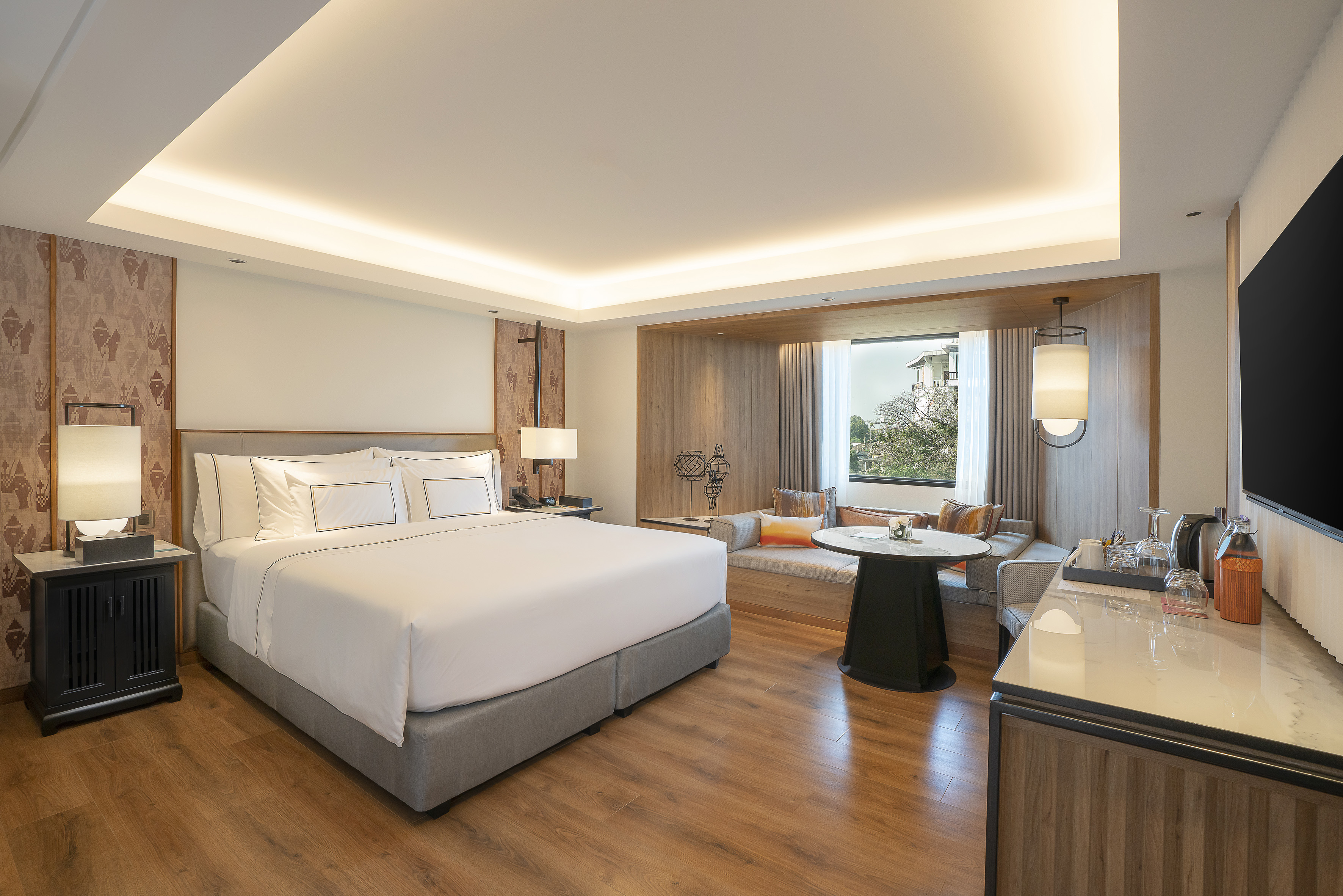 Modern luxury hotel room with king bed and cozy window lounge.