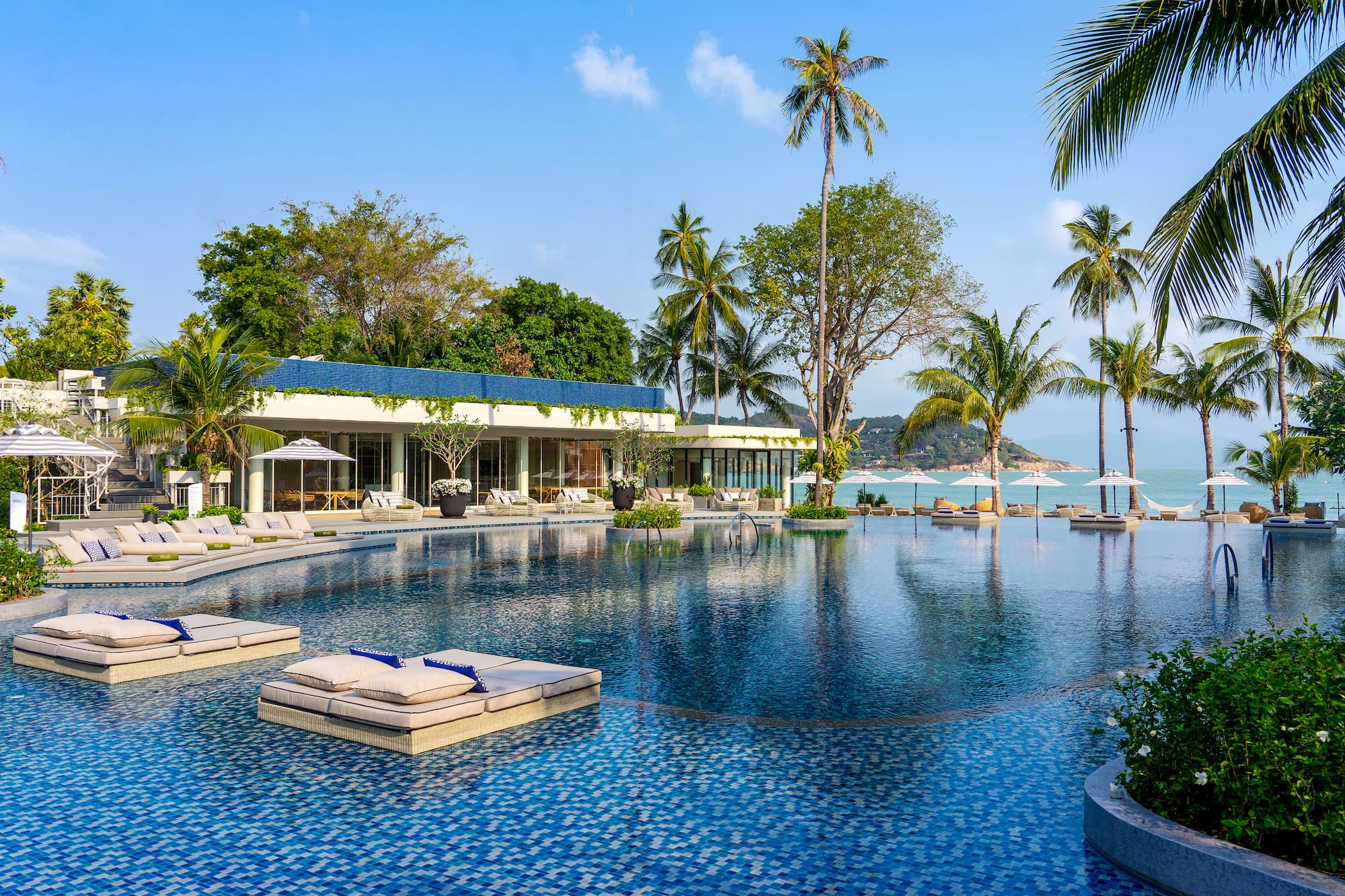 Luxury tropical resort with large swimming pool, palm trees, and ocean view.