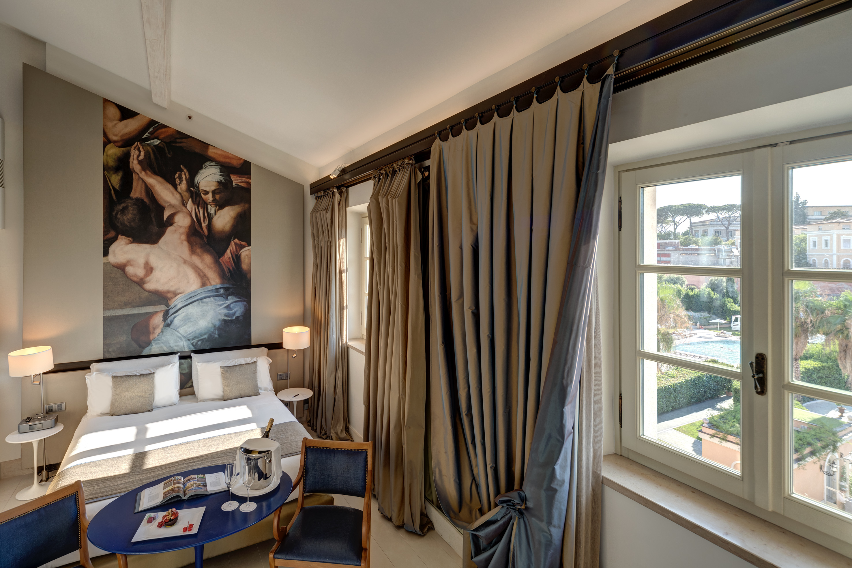 Elegant hotel bedroom, classical mural, champagne, pool view.
