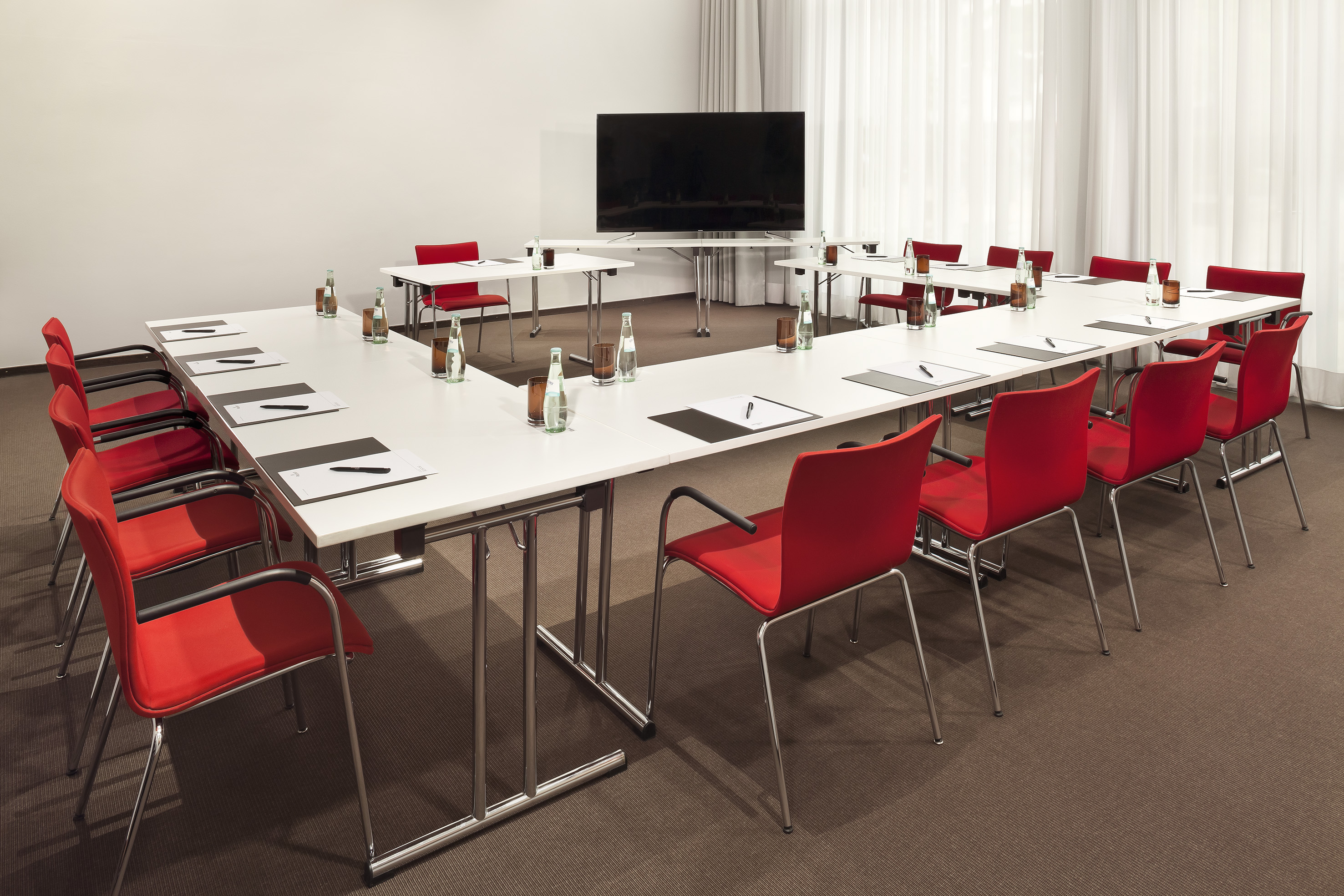 Professional conference room with U-shaped table, red chairs, and presentation screen.