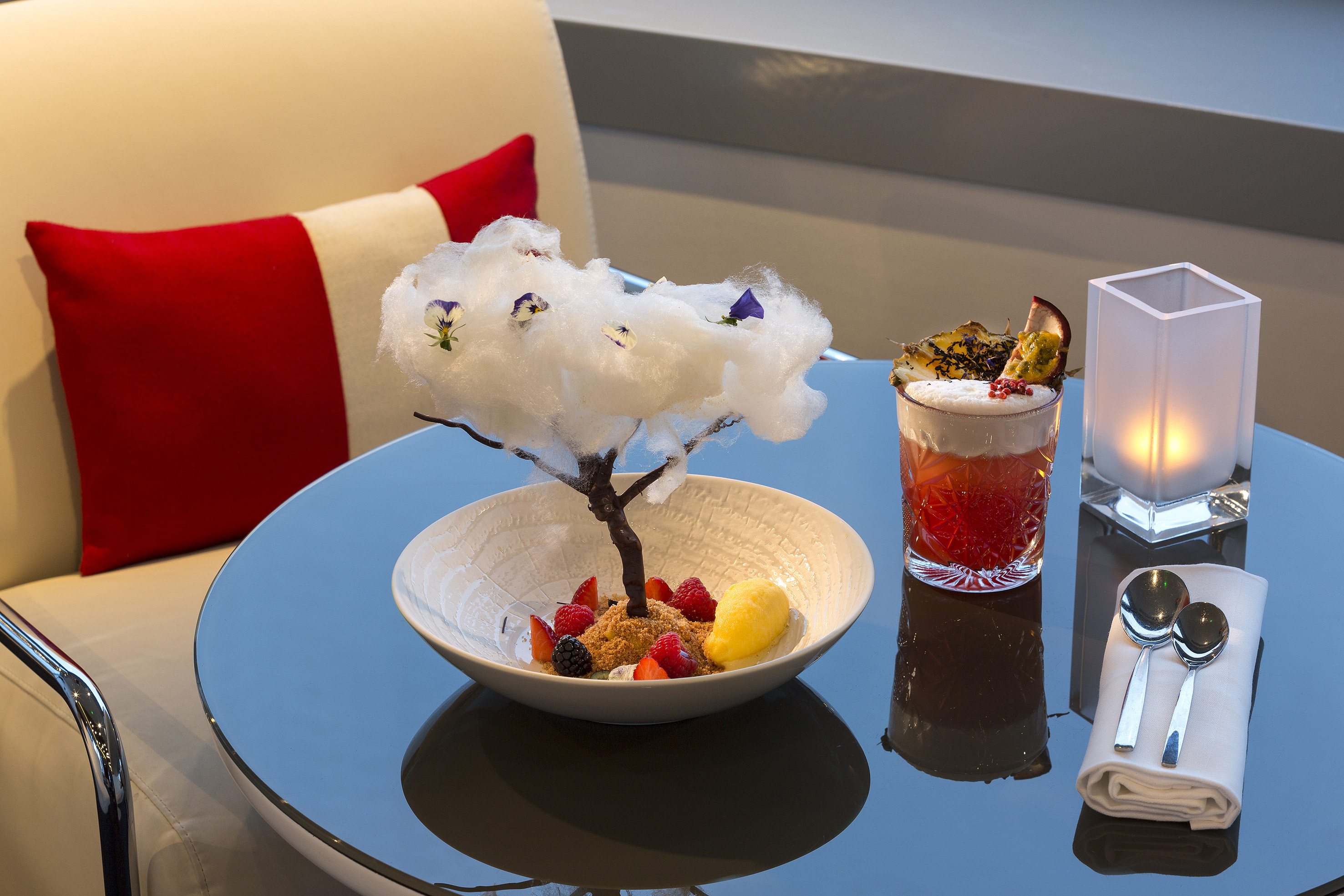 Cotton candy tree dessert with berries, sorbet, and garnished cocktail on a table.