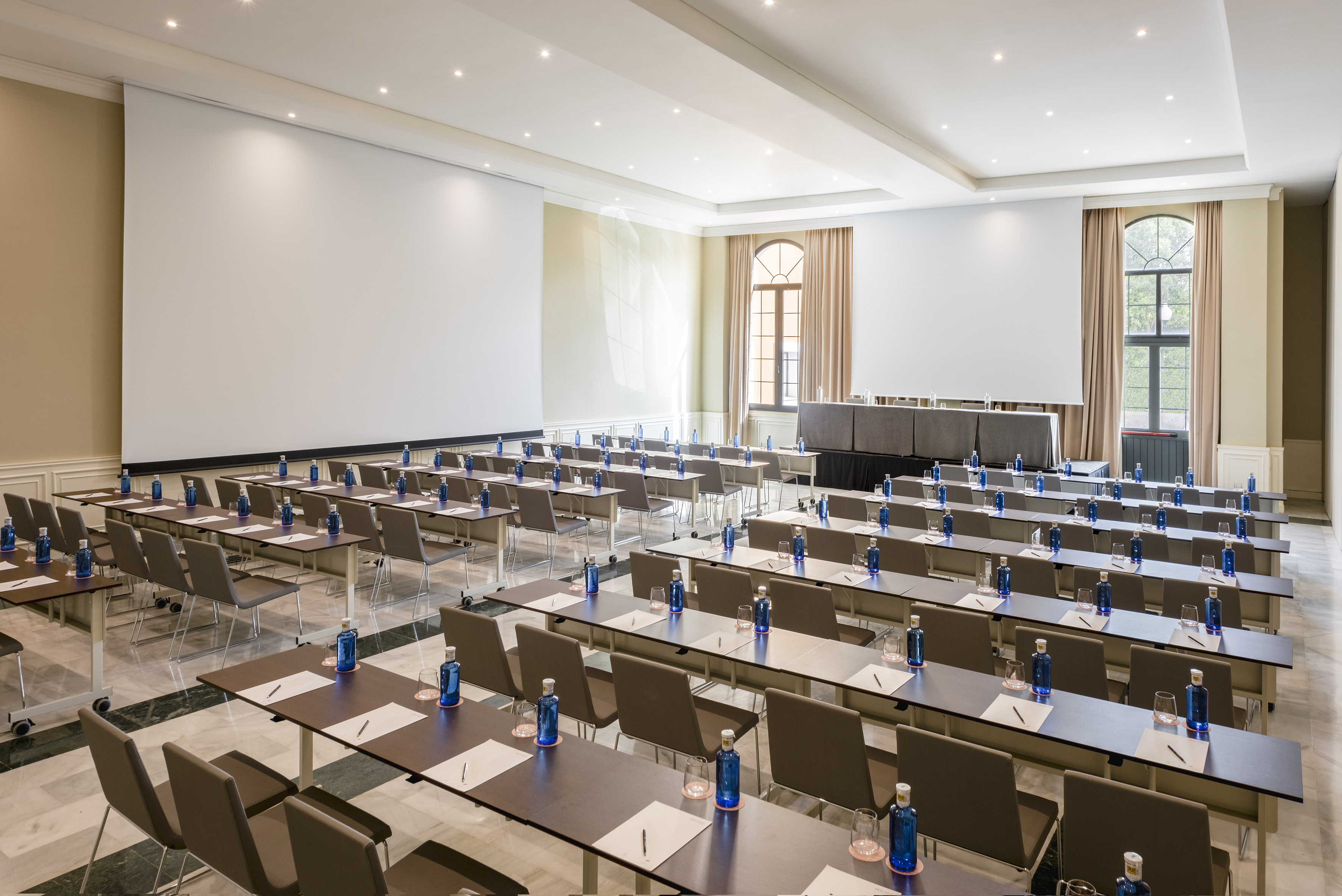 Conference room with classroom setup, tables, chairs, water bottles, screen.
