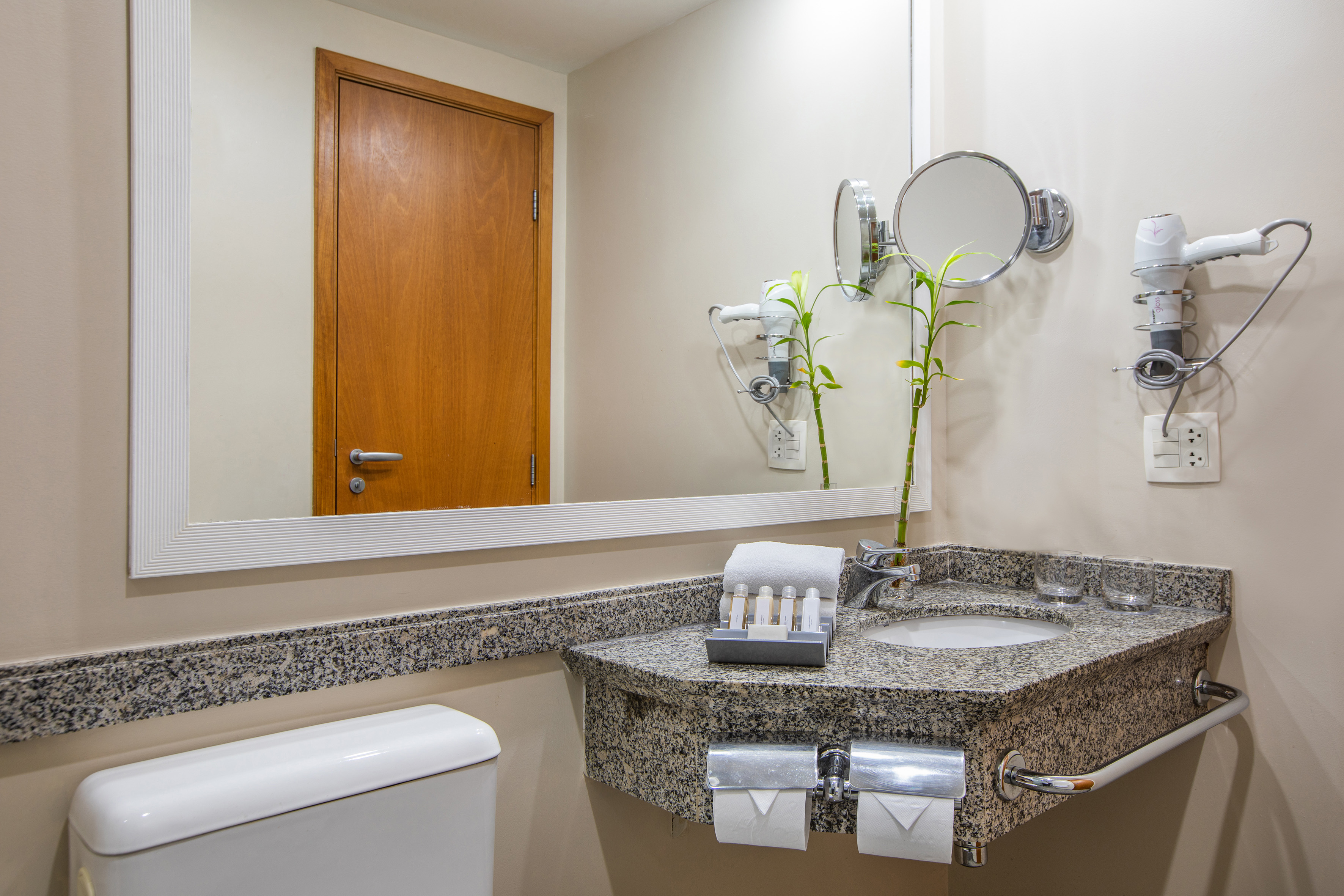 Hotel bathroom with granite vanity, sink, mirror, toilet, and amenities.