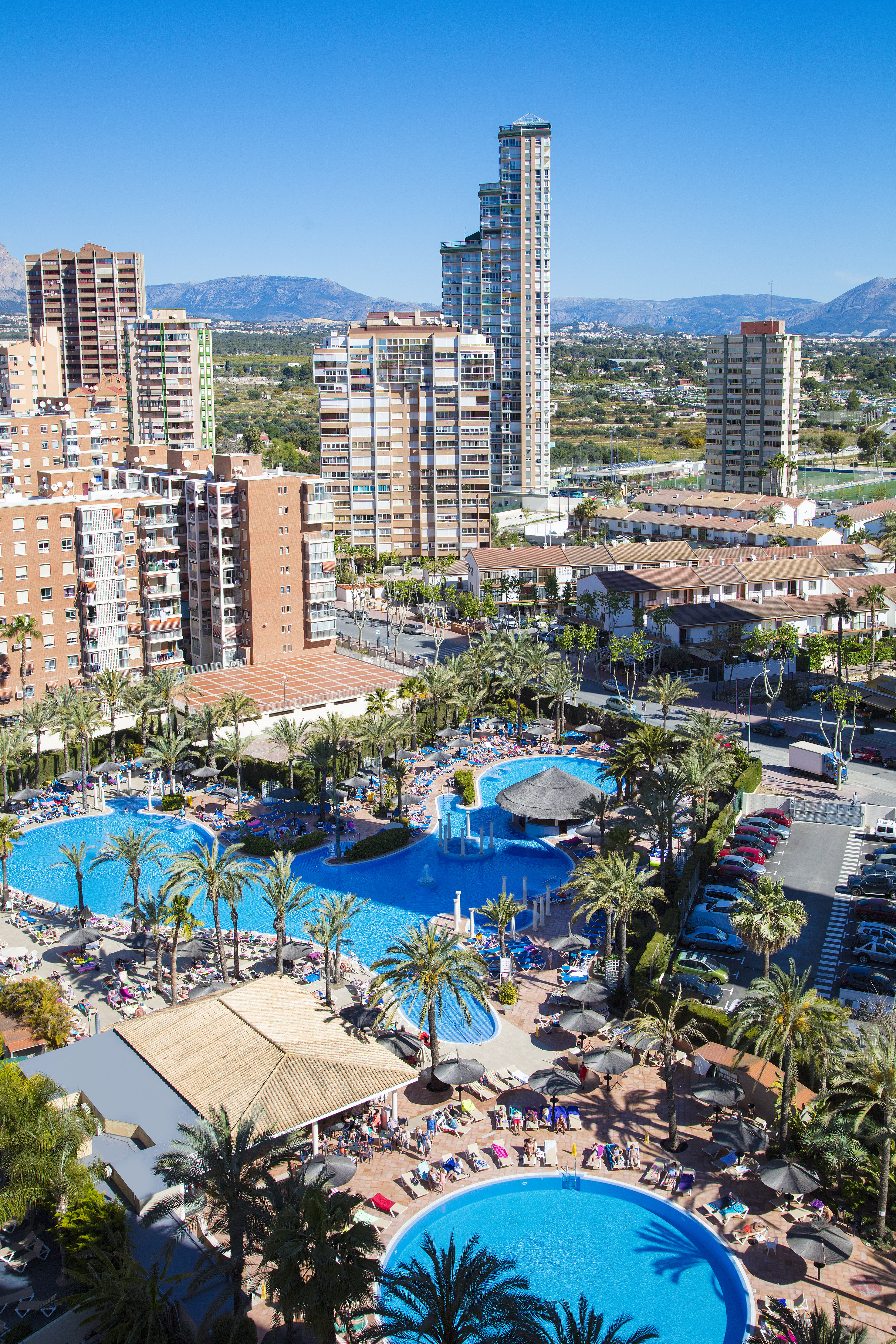 Benidorm resort pools, palm trees, hotel skyline, mountains.