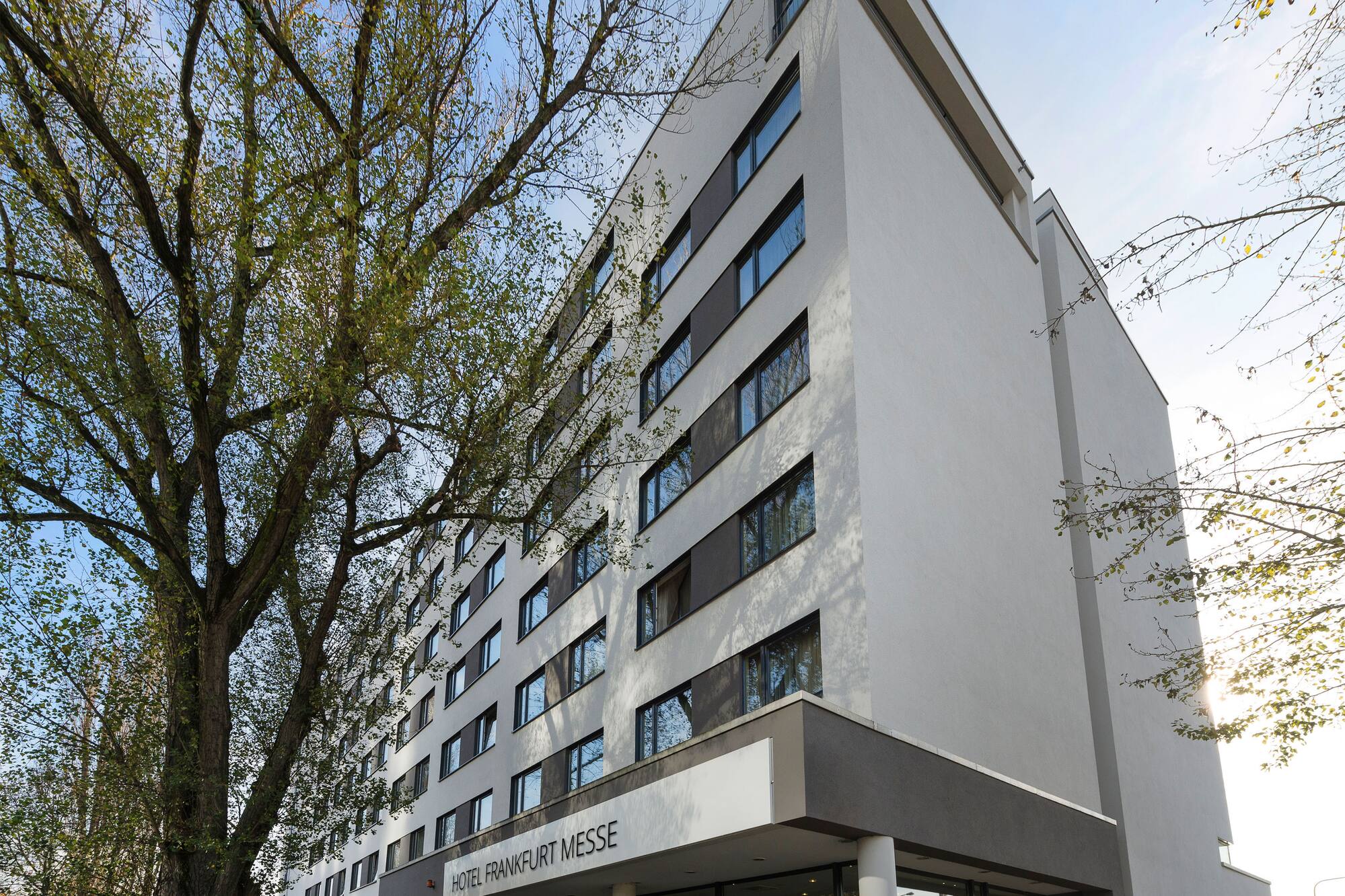 Hotel Frankfurt Messe modern building exterior with large tree.