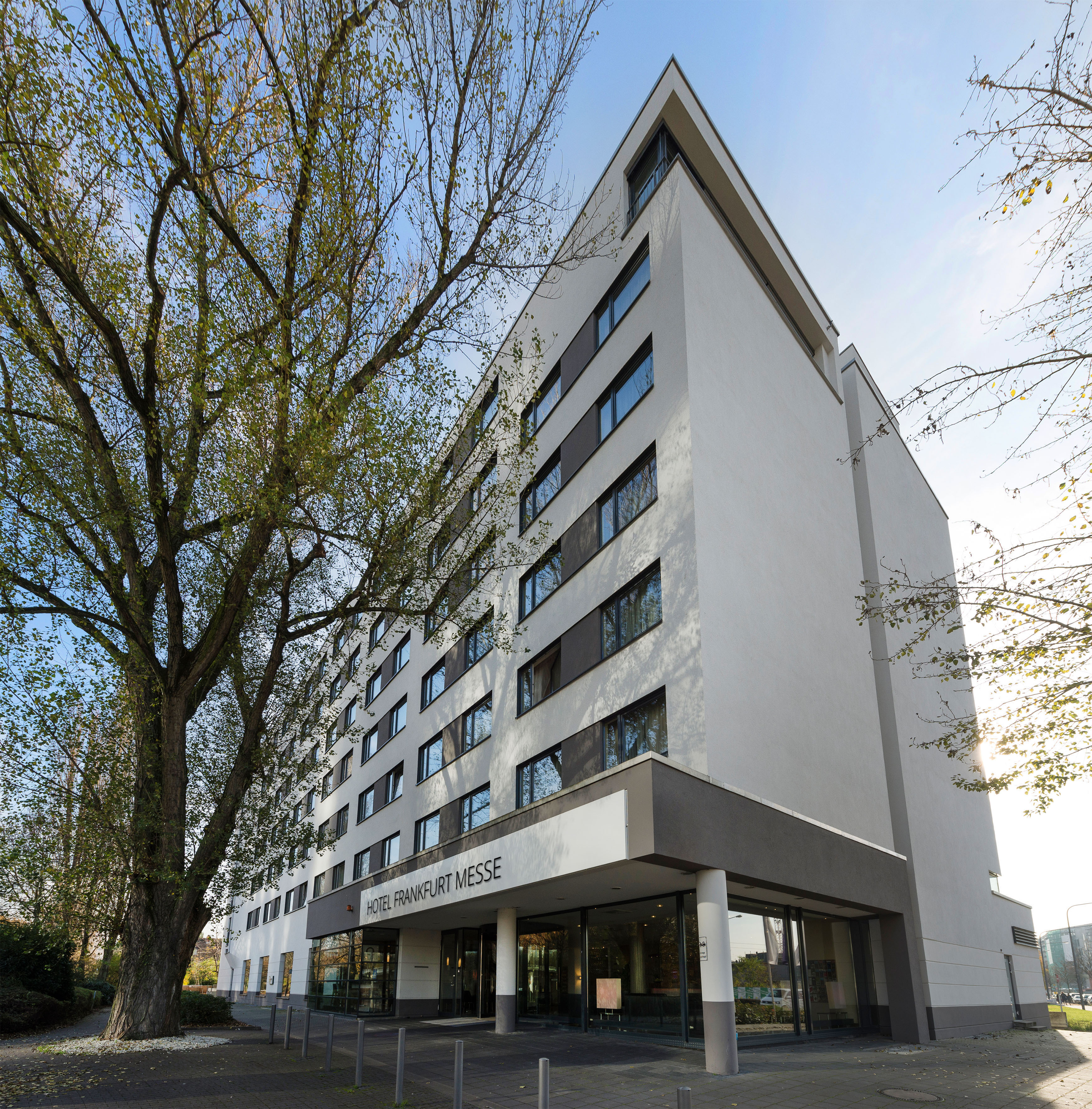 Hotel Frankfurt Messe modern building exterior with large tree.