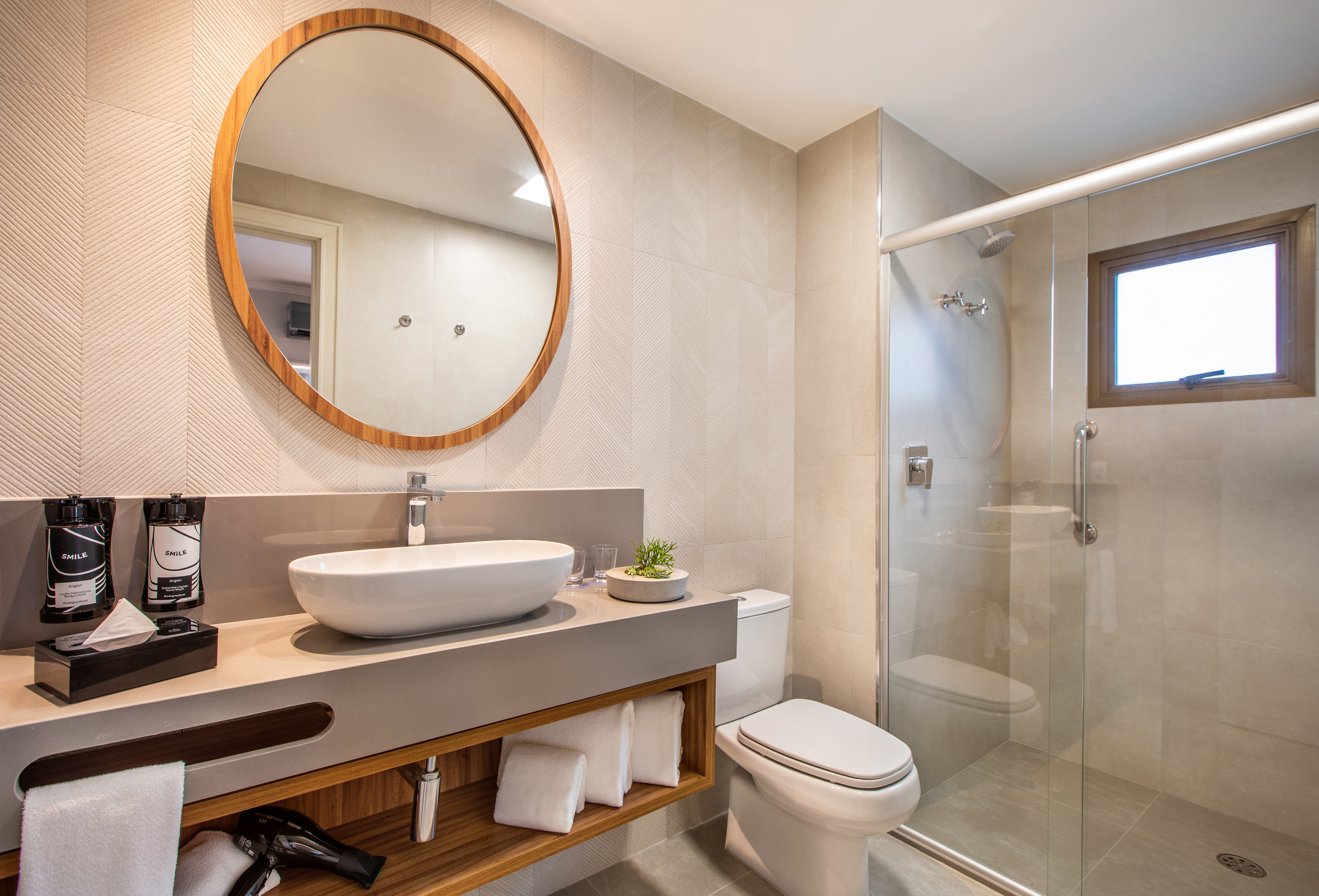 Clean modern bathroom with round mirror, vessel sink, vanity, toilet, and glass shower.