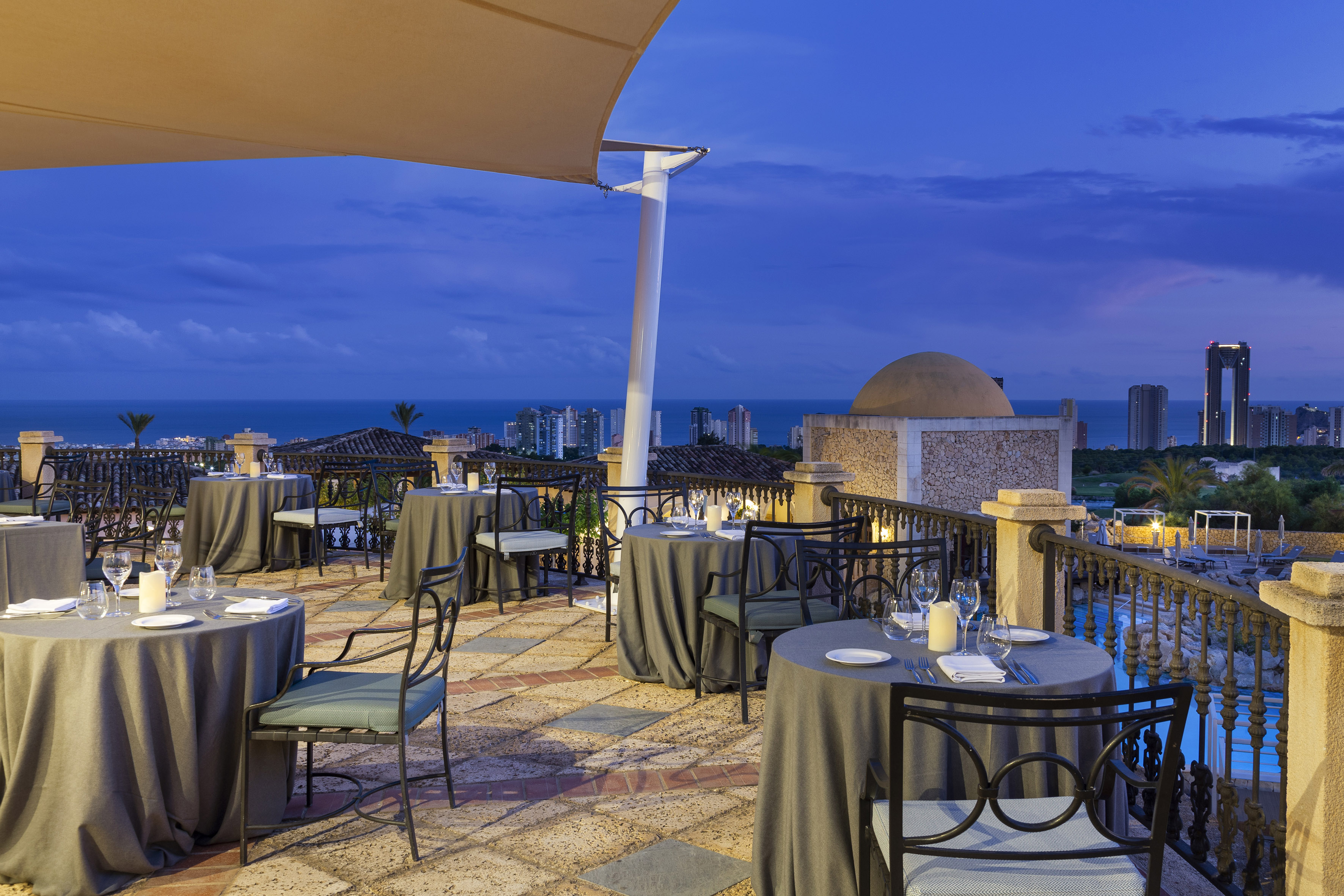 Rooftop restaurant terrace at dusk with ocean view and city skyline.