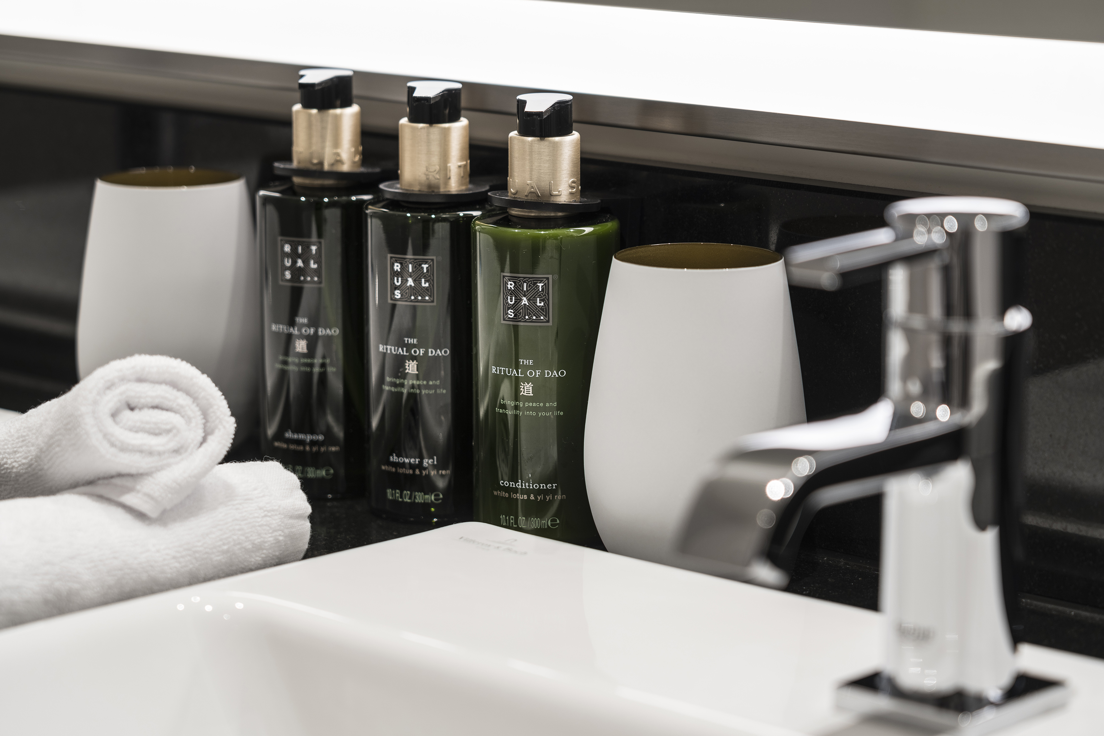 Rituals of Dao shampoo, conditioner, shower gel, white towels, and faucet.