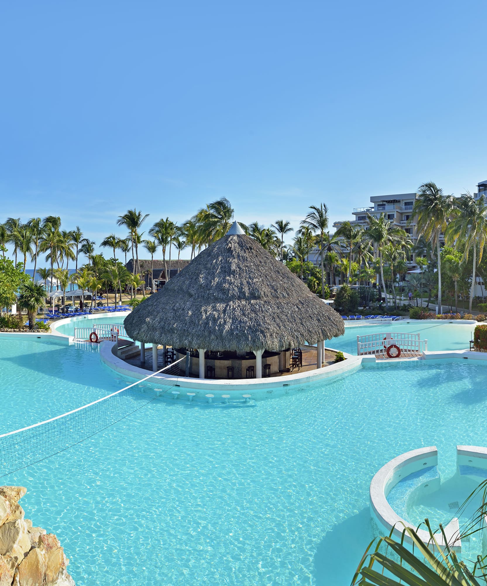 a pool with a thatched roof and a building in the background