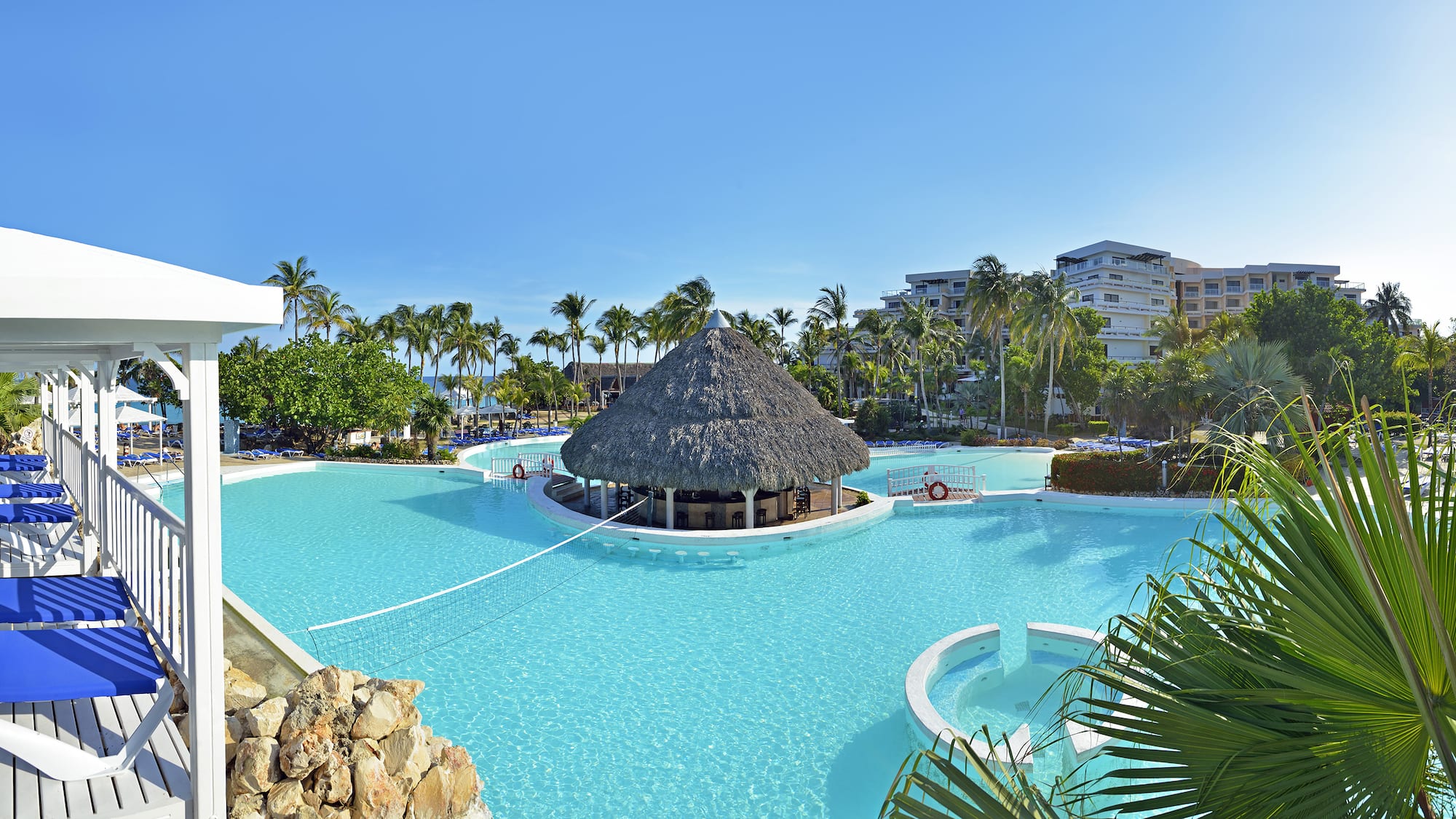 a pool with a thatched roof and a building in the background