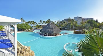 a pool with a thatched roof and a building in the background