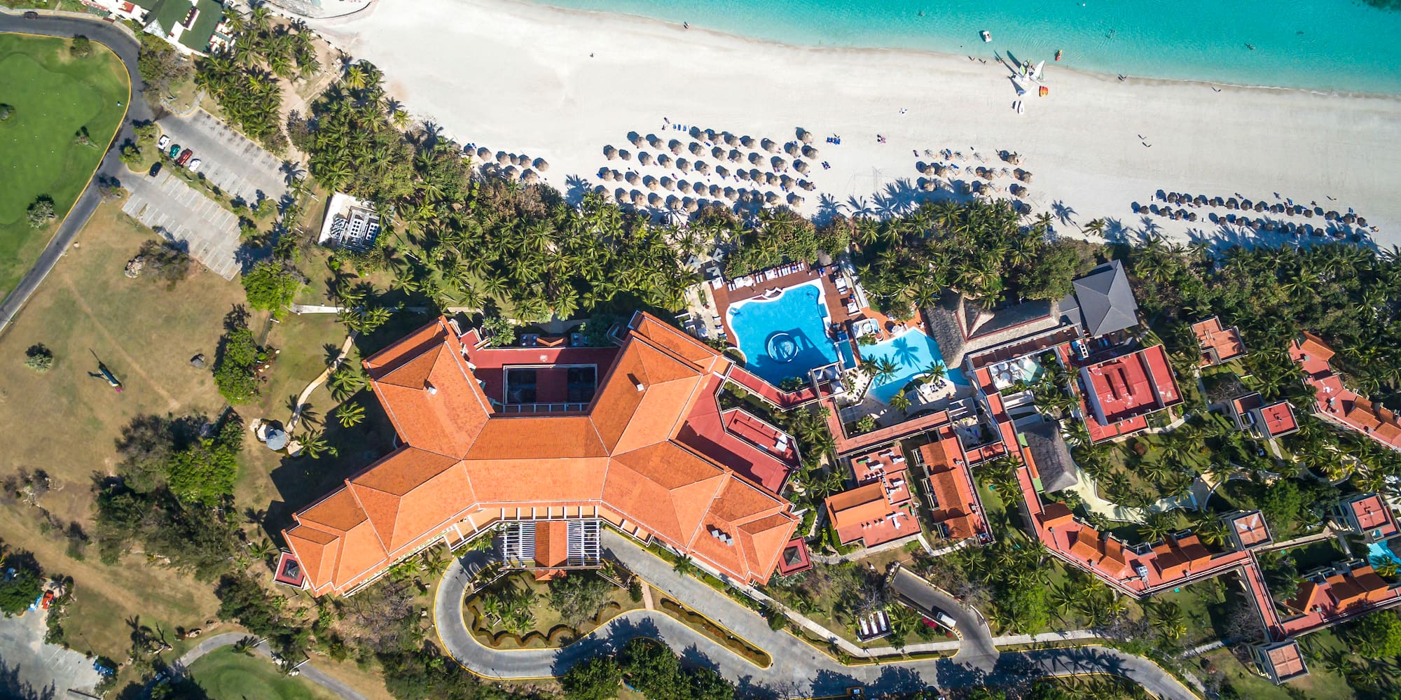 a large building with a pool and trees on a beach