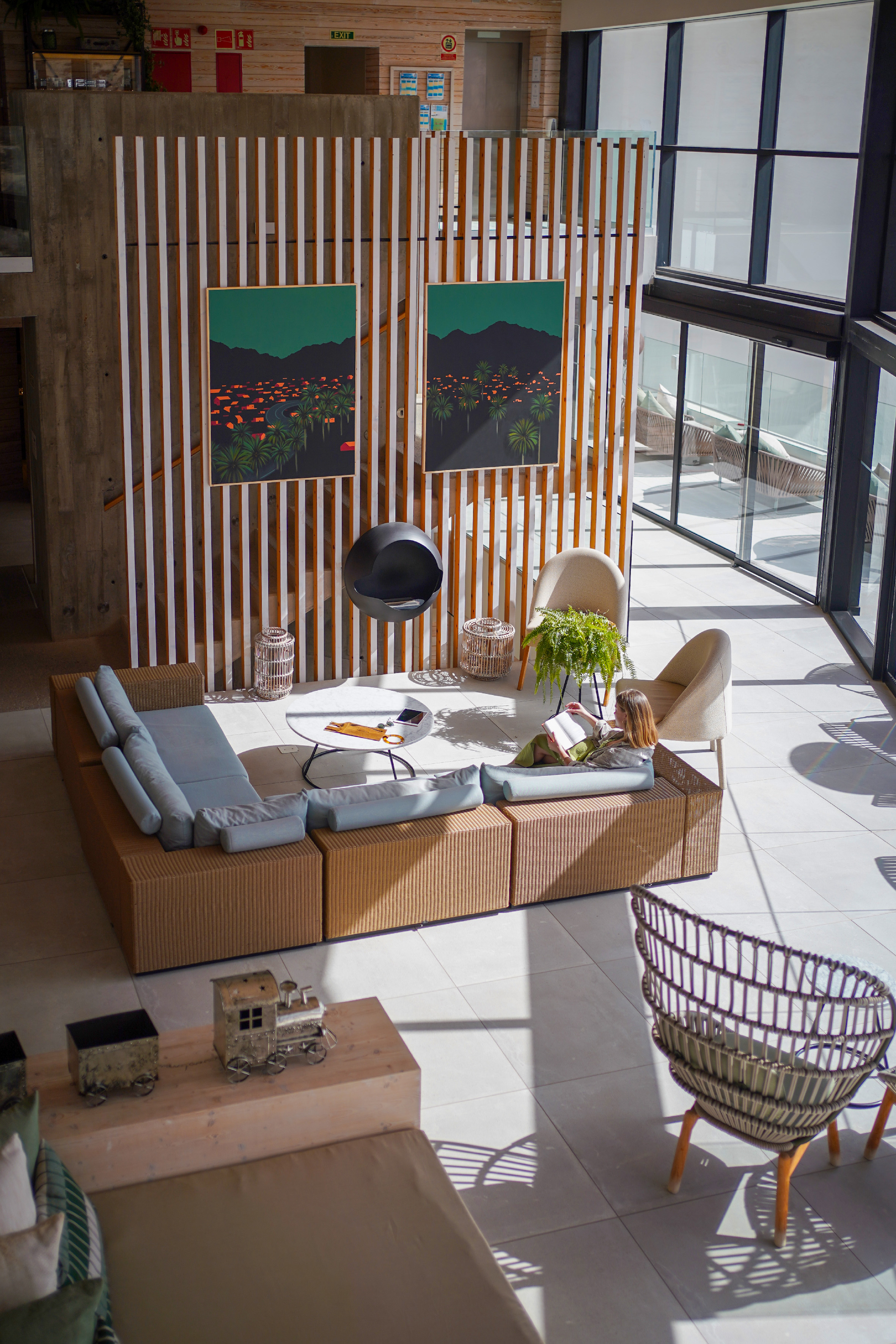 Contemporary hotel lobby lounge with woman reading on modular sofa, modern art.
