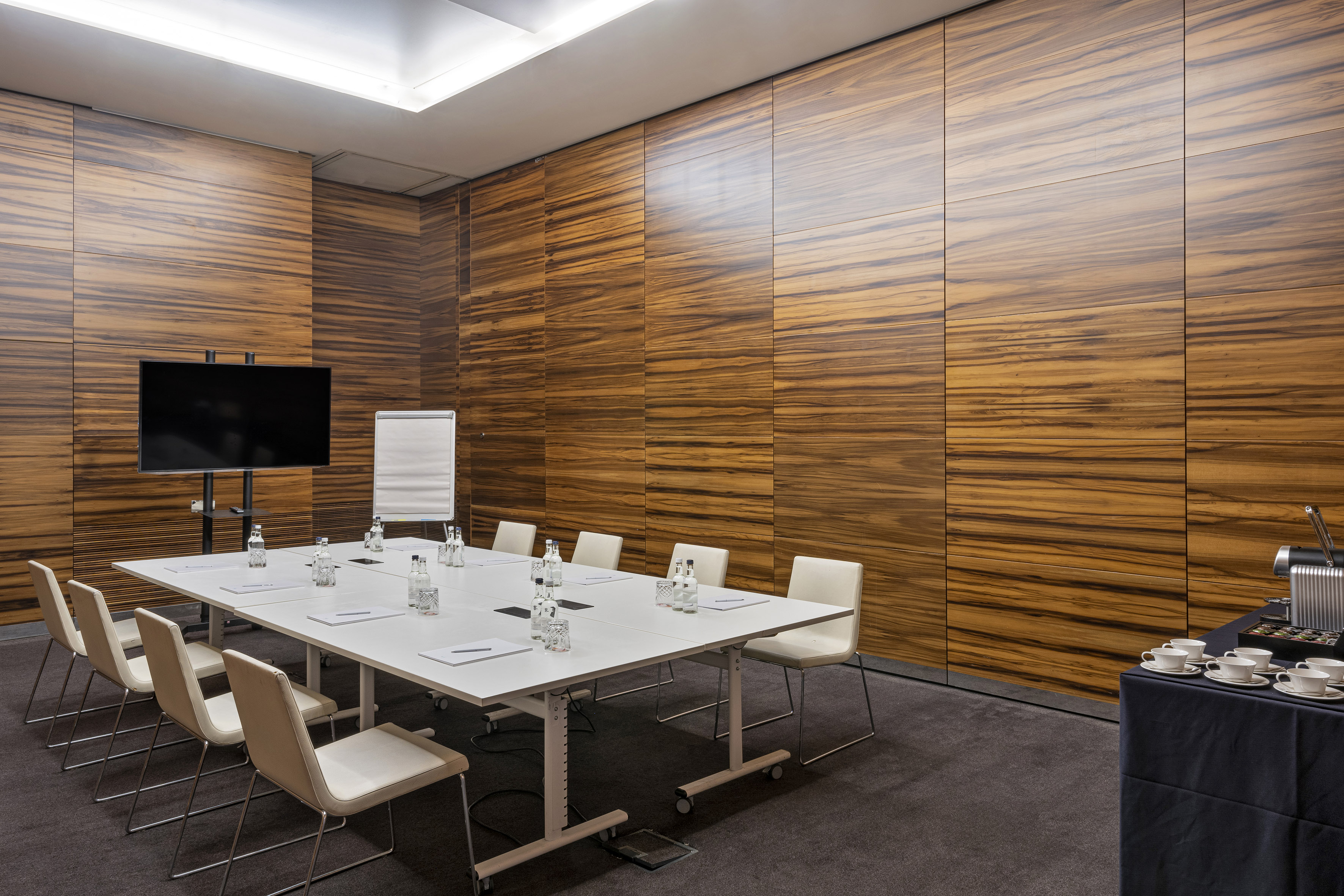Modern conference room with wood walls, presentation screen, and coffee station.