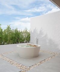 a bathtub outside with a white wall and plants
