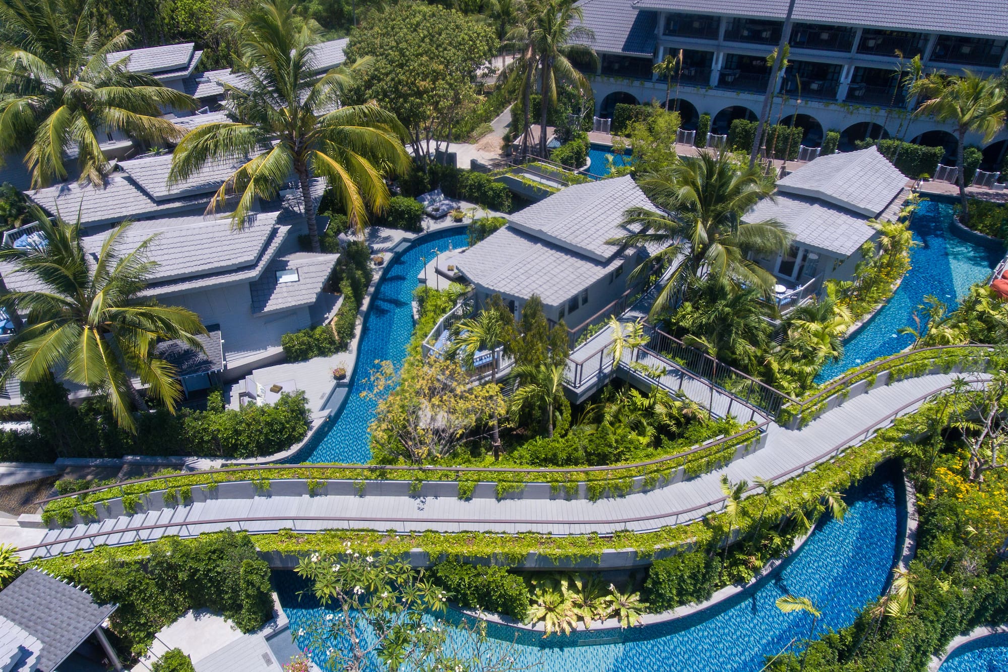 Luxury tropical resort aerial view with villas, winding pools, and elevated walkways.