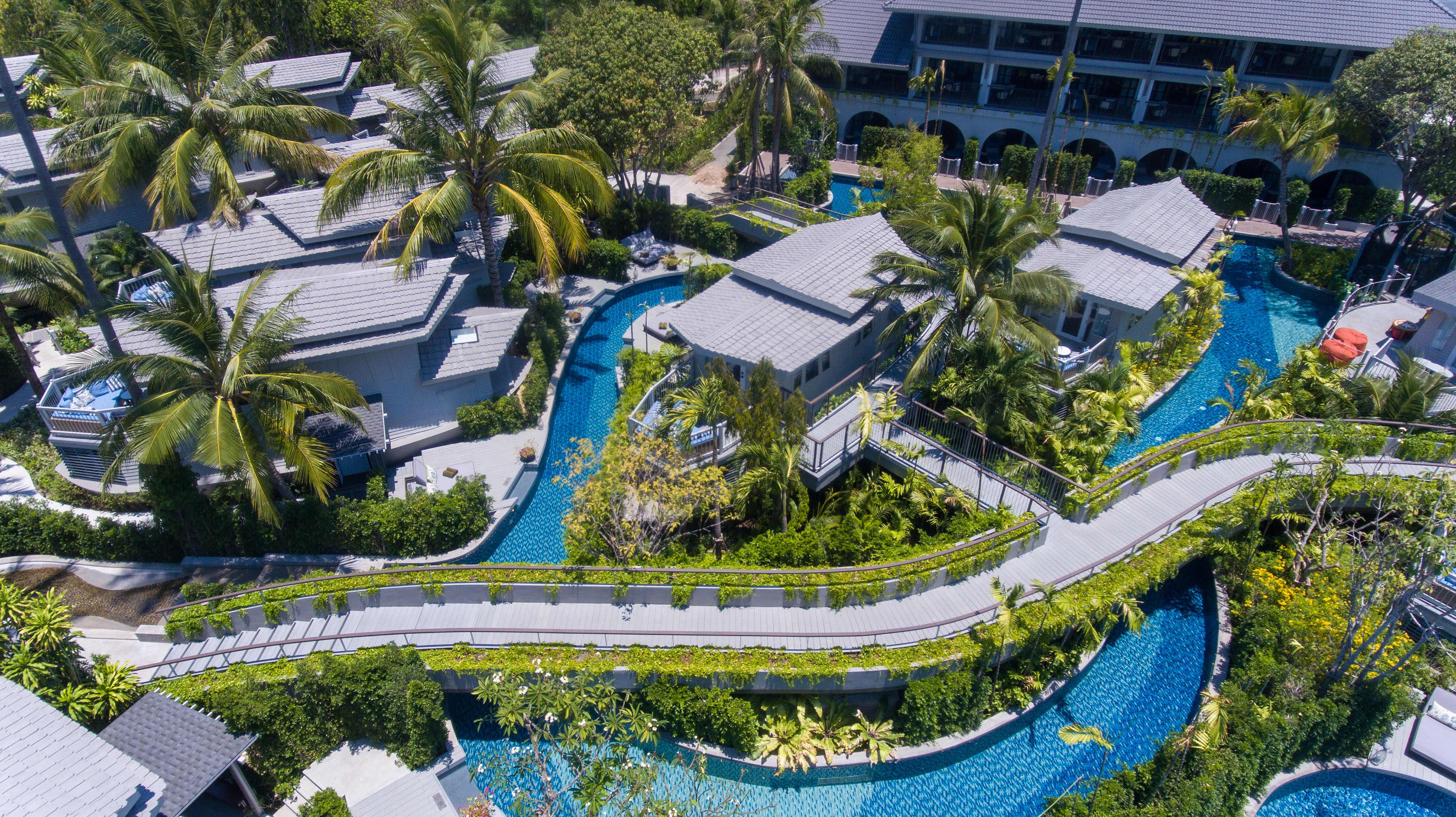 Luxury tropical resort aerial view with villas, winding pools, and elevated walkways.
