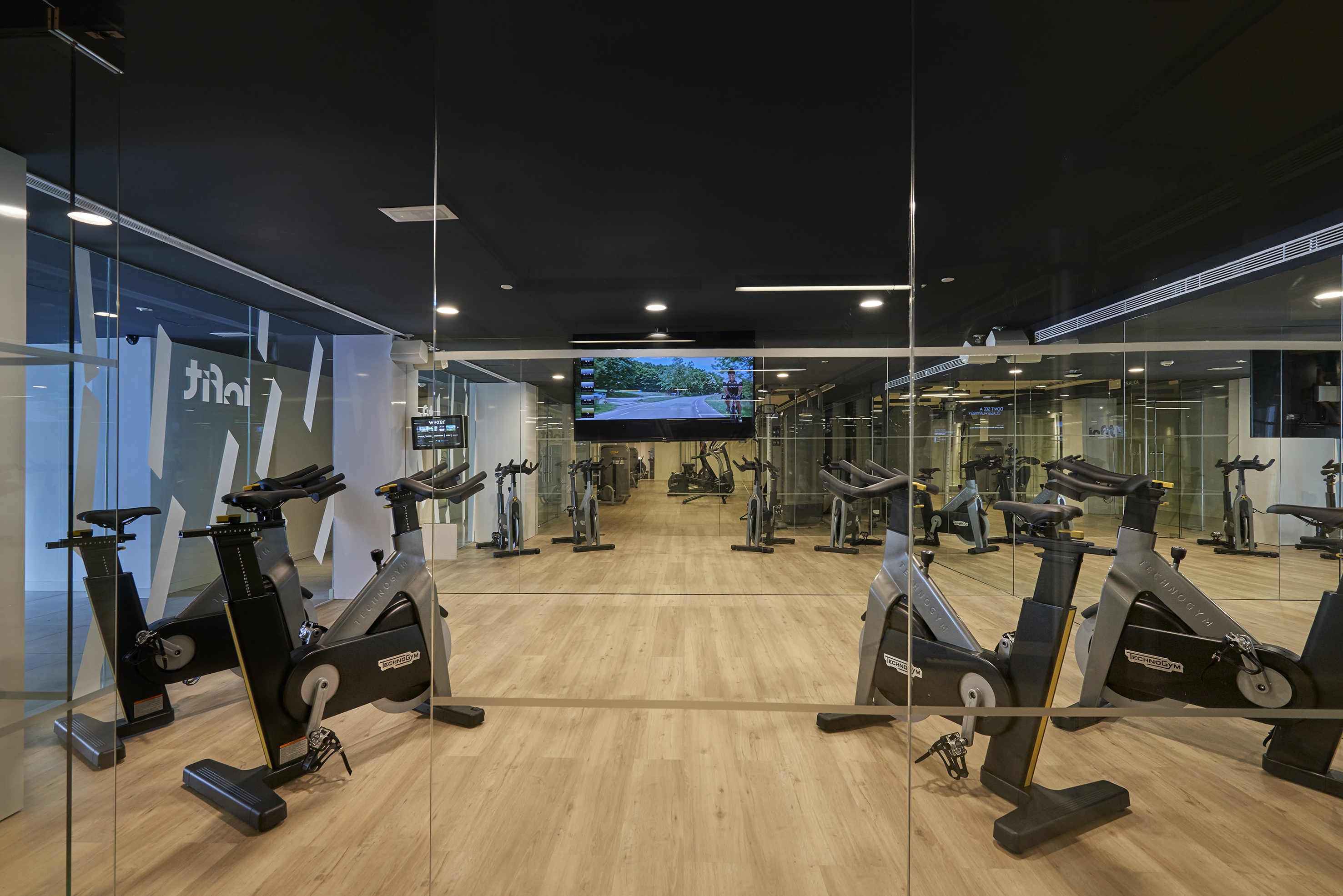 Sleek gym spin studio with Technogym exercise bikes and virtual cycling screen.