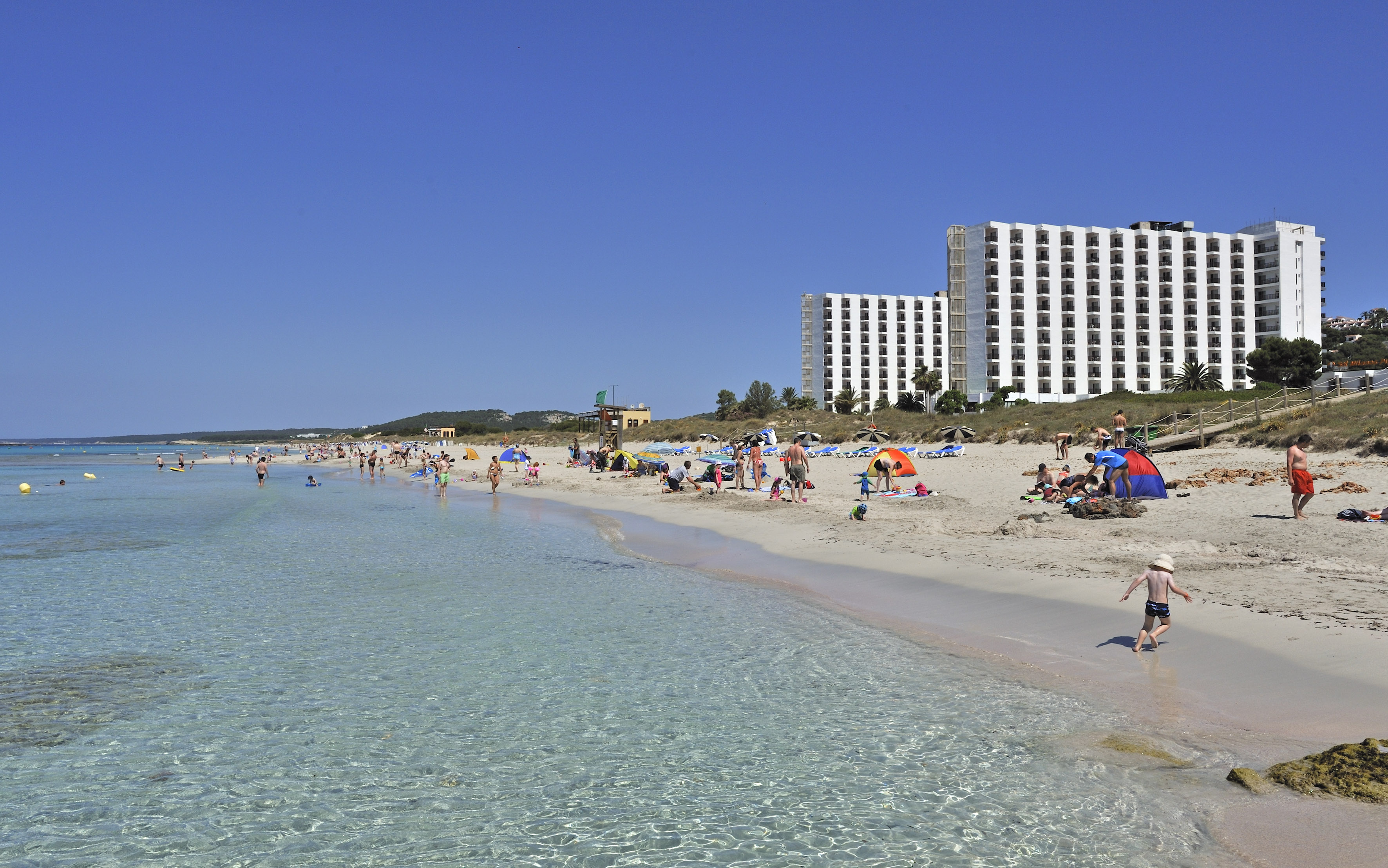 Clear turquoise water beach, white resort hotels, families vacationing.
