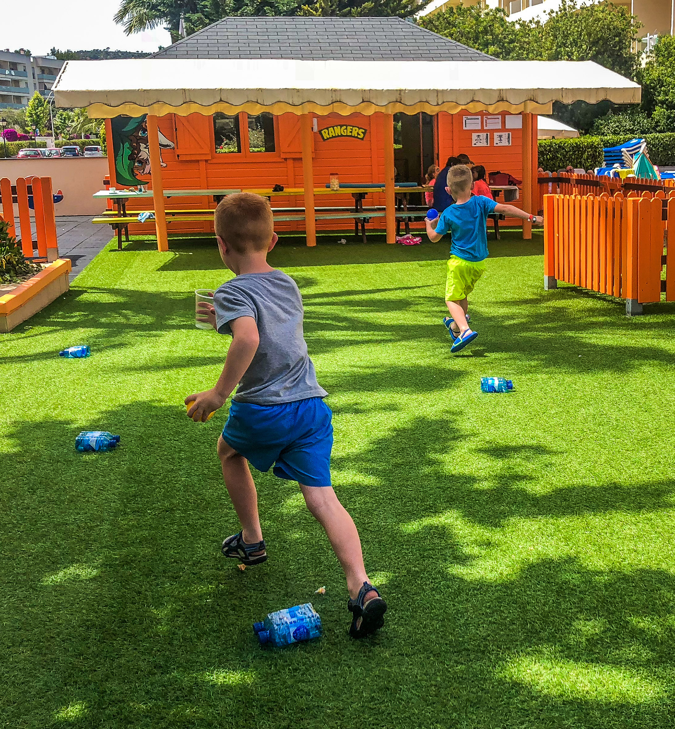 Boys running on green artificial grass near 'Rangers' kids' clubhouse, playground.