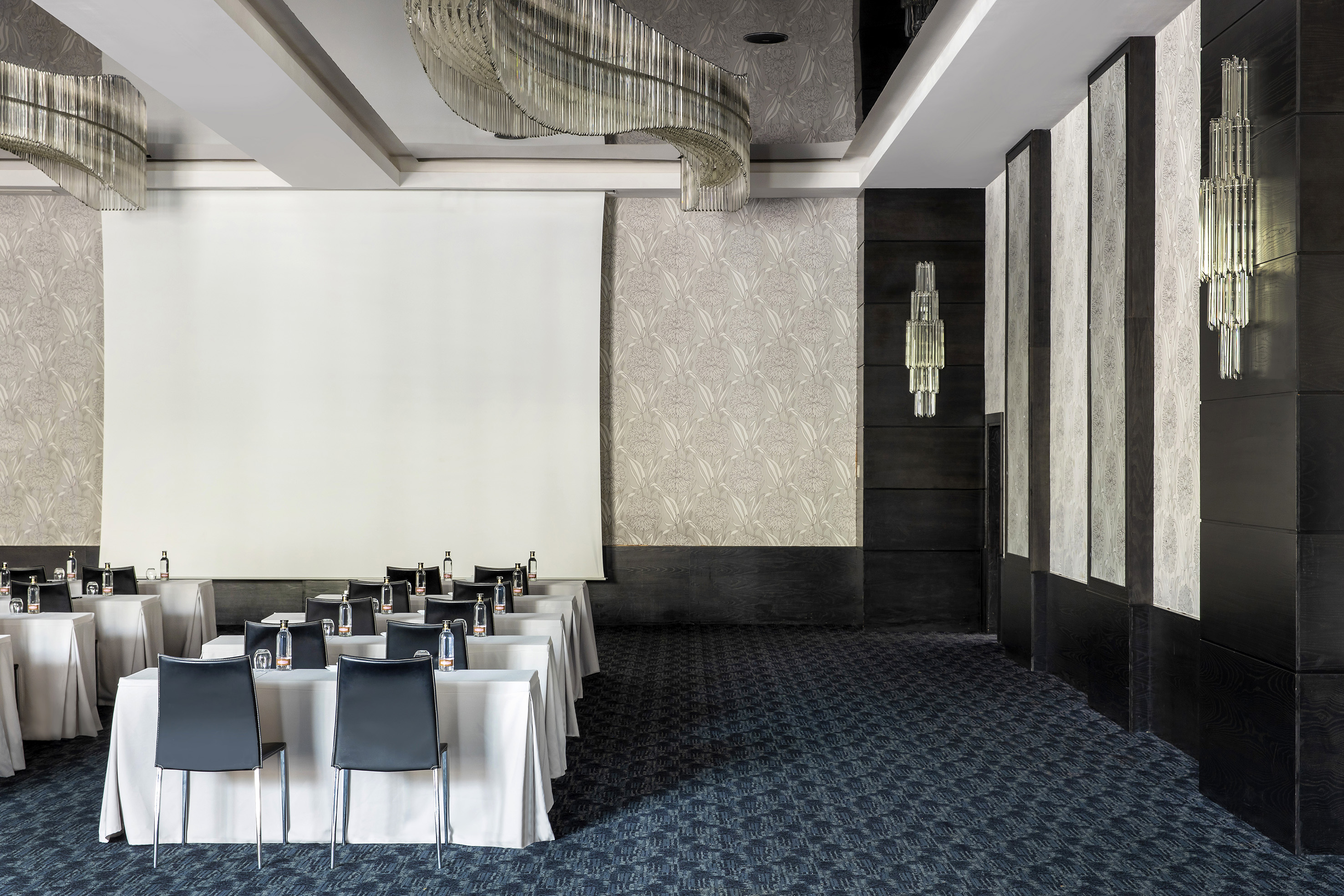 Modern meeting room with projection screen, set tables, and stylish chandeliers.