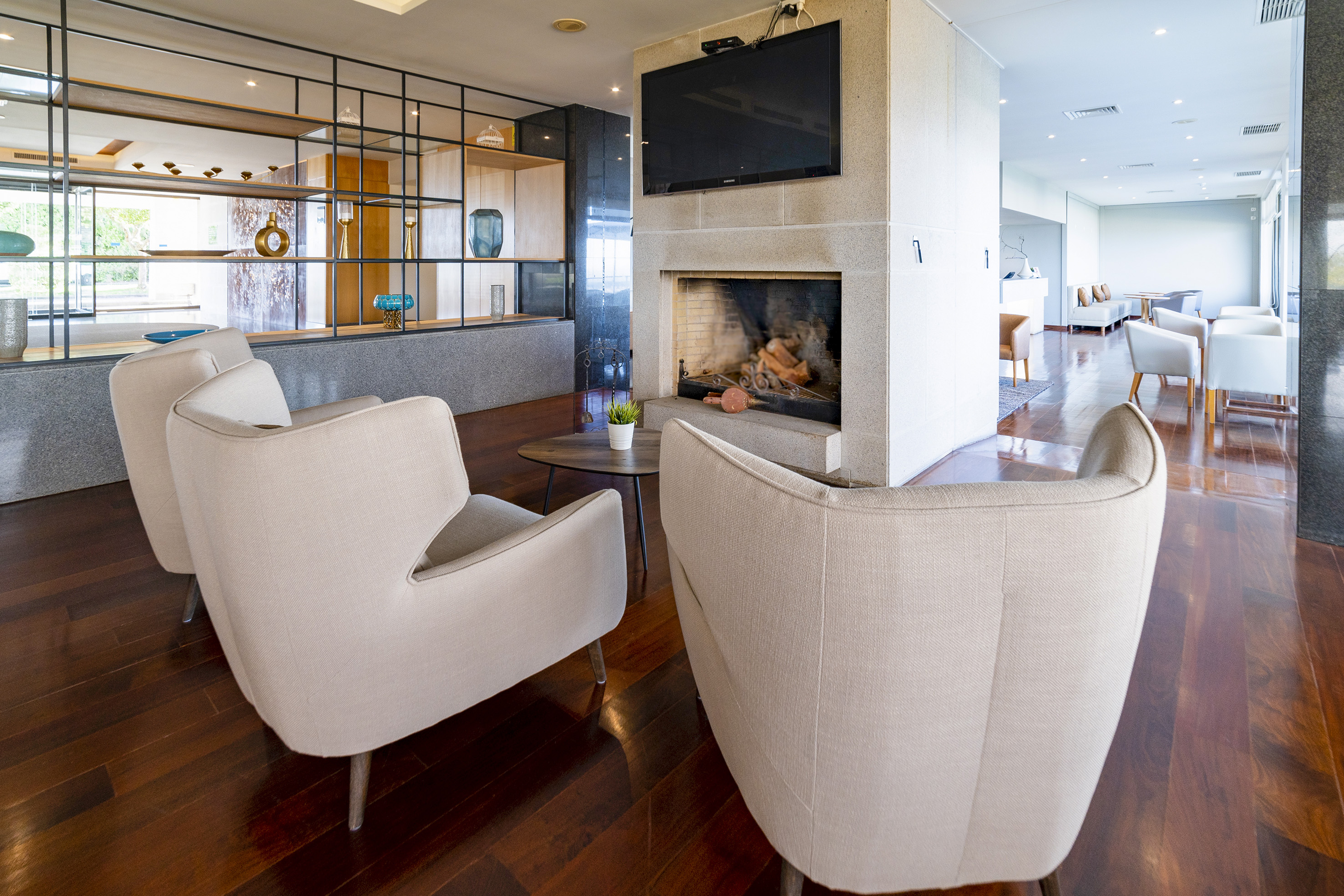 Hotel lounge with fireplace, TV, cream armchairs, and modern wood floor.